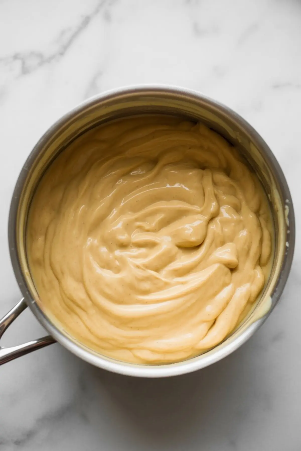 Smooth, creamy eggnog fudge mixture in a saucepan after cooking, with a rich golden-beige color and glossy texture, ready to be poured into a mold.
