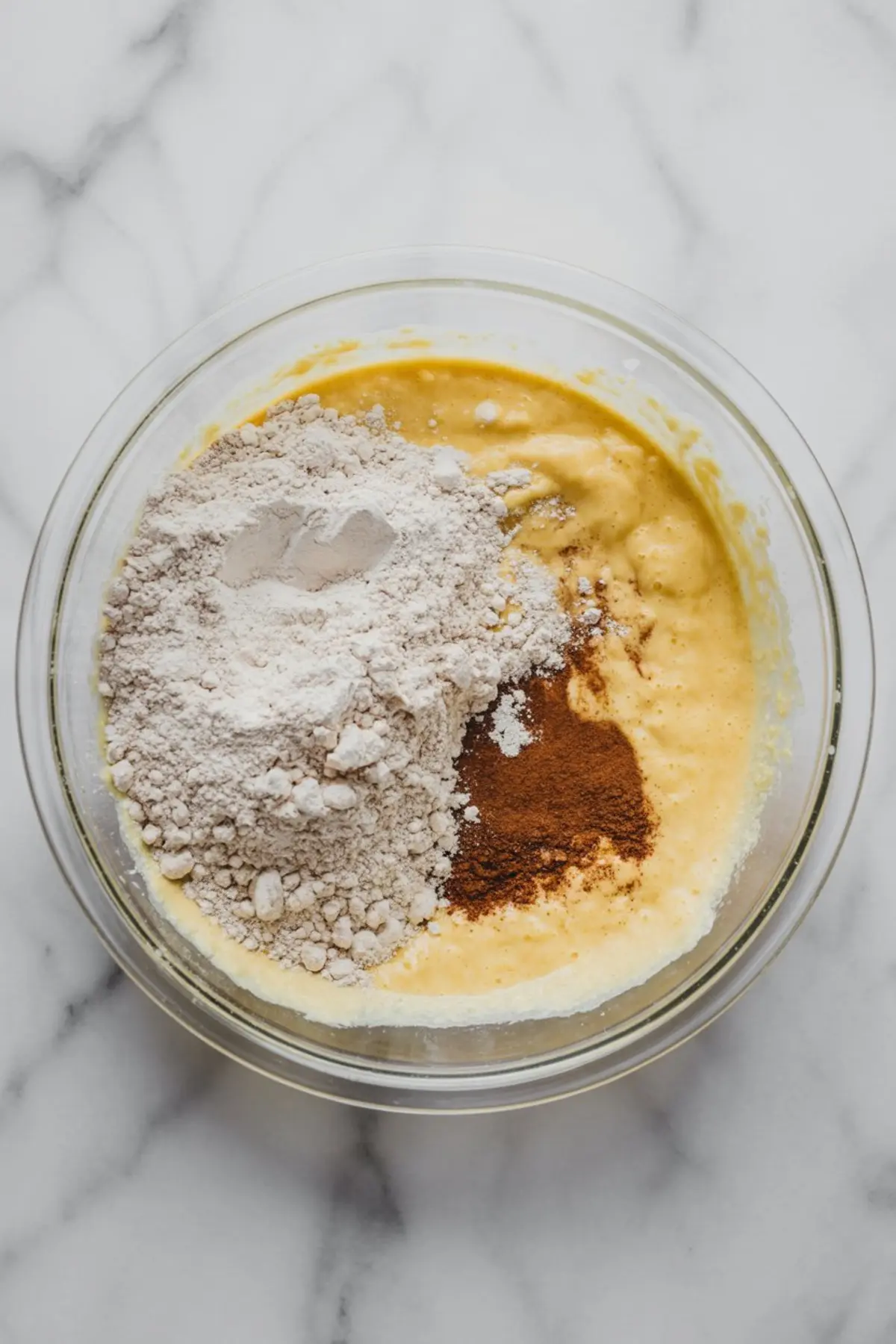 Top-down view of snickerdoodle cookie batter in a mixing bowl, with flour and ground cinnamon just added on top, ready to be mixed.