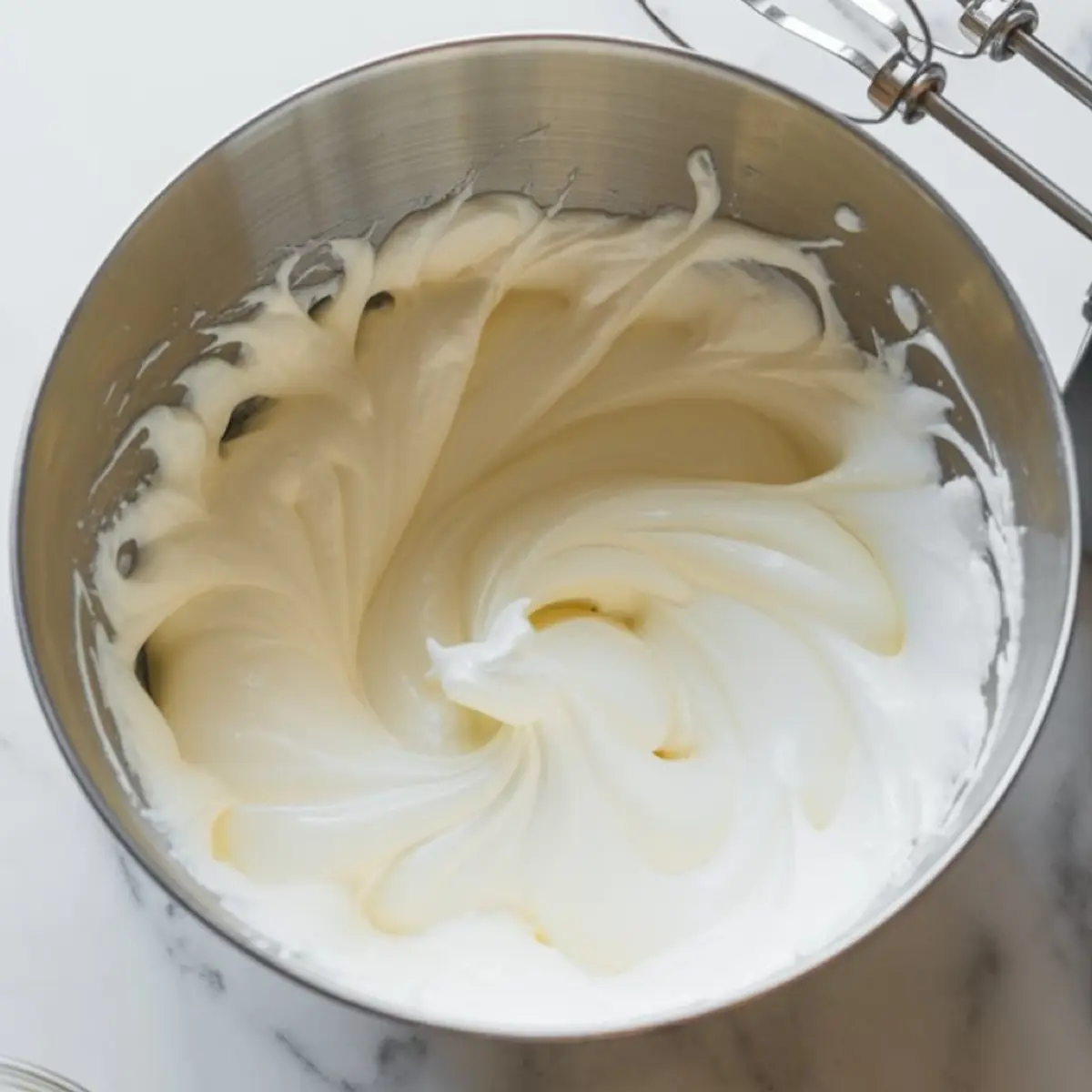 Whipped egg whites forming stiff peaks in a metal mixing bowl, just finished with a hand mixer.