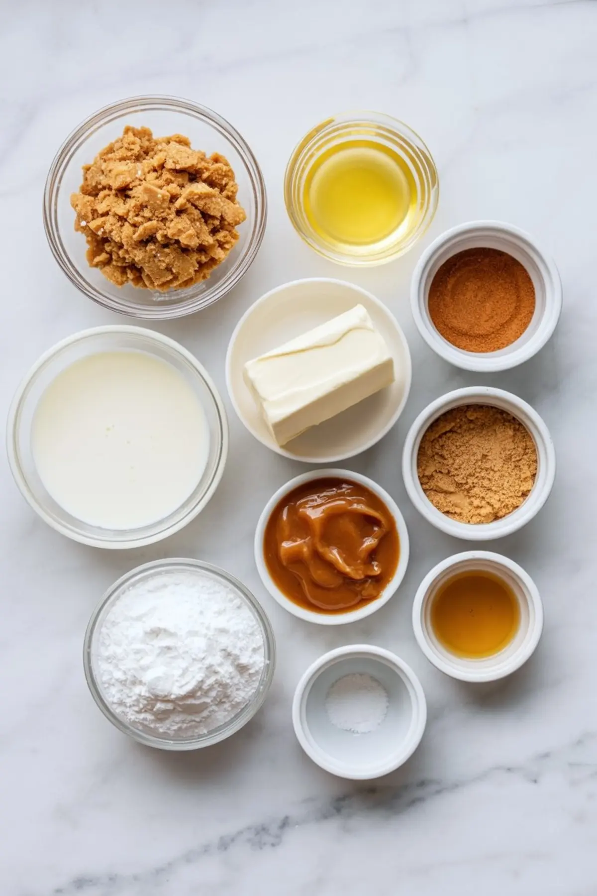 Flat lay of mousse ingredients including cream, brown sugar, butter, caramel, powdered sugar, vanilla extract, gingerbread crumbs, and warm spices in small bowls.
