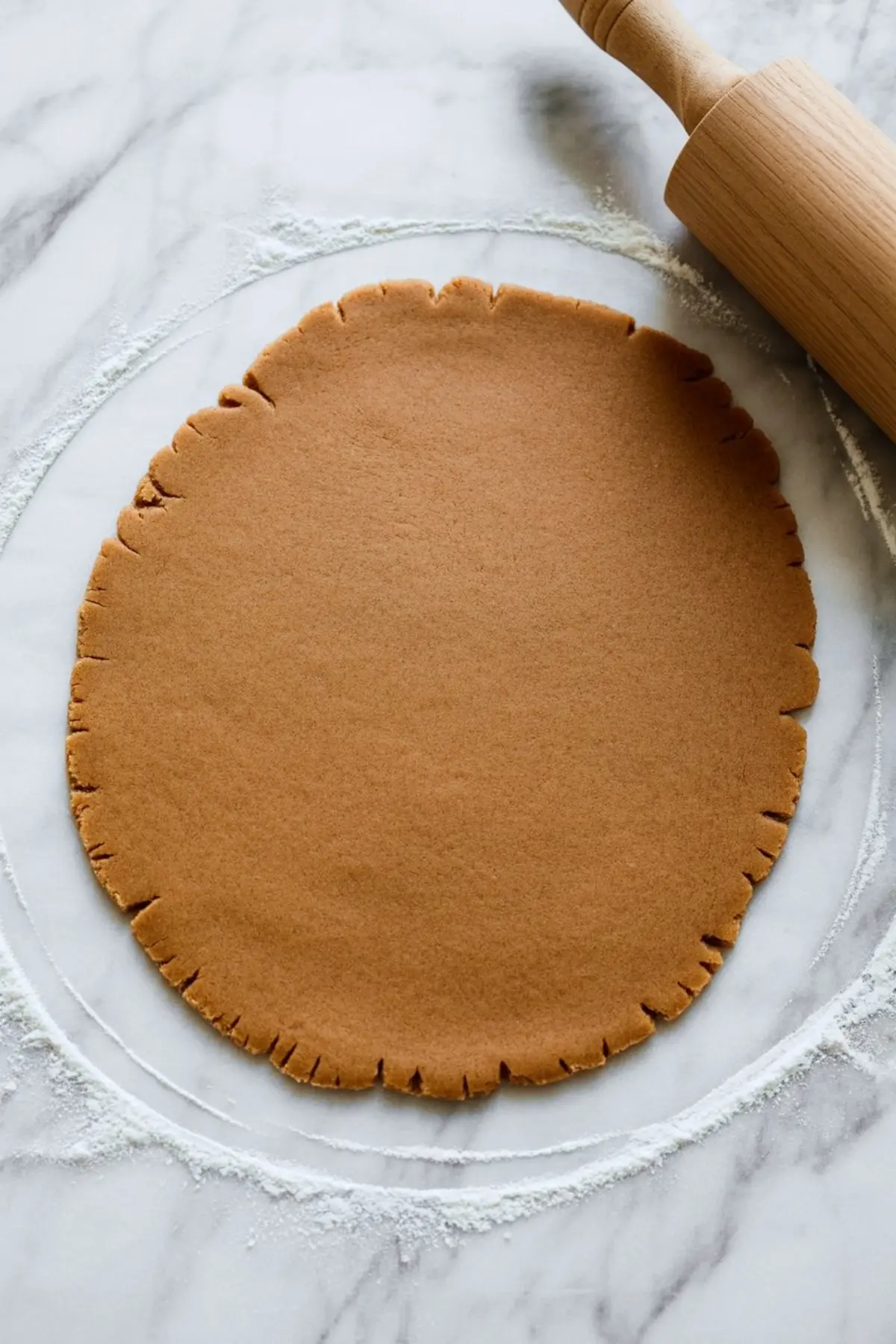 Rolled-out gingerbread cookie dough rests on a floured marble countertop with a wooden rolling pin placed nearby.