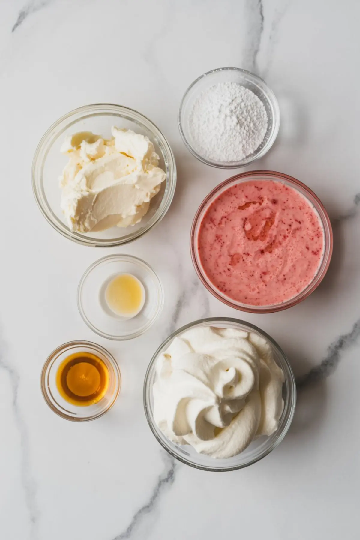 Image displays separated ingredients in clear glass bowls, including whipped cream cheese, powdered sugar, strawberry puree, vanilla extract, and whipped topping arranged neatly on a white marble surface.
