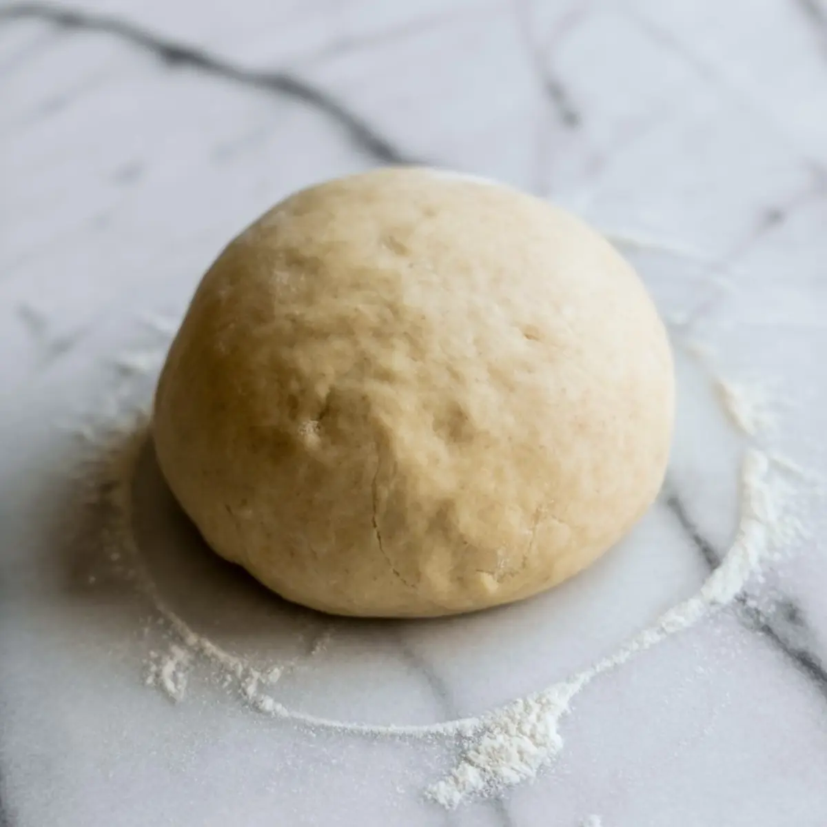 A smooth ball of dough rests on a lightly floured marble surface.