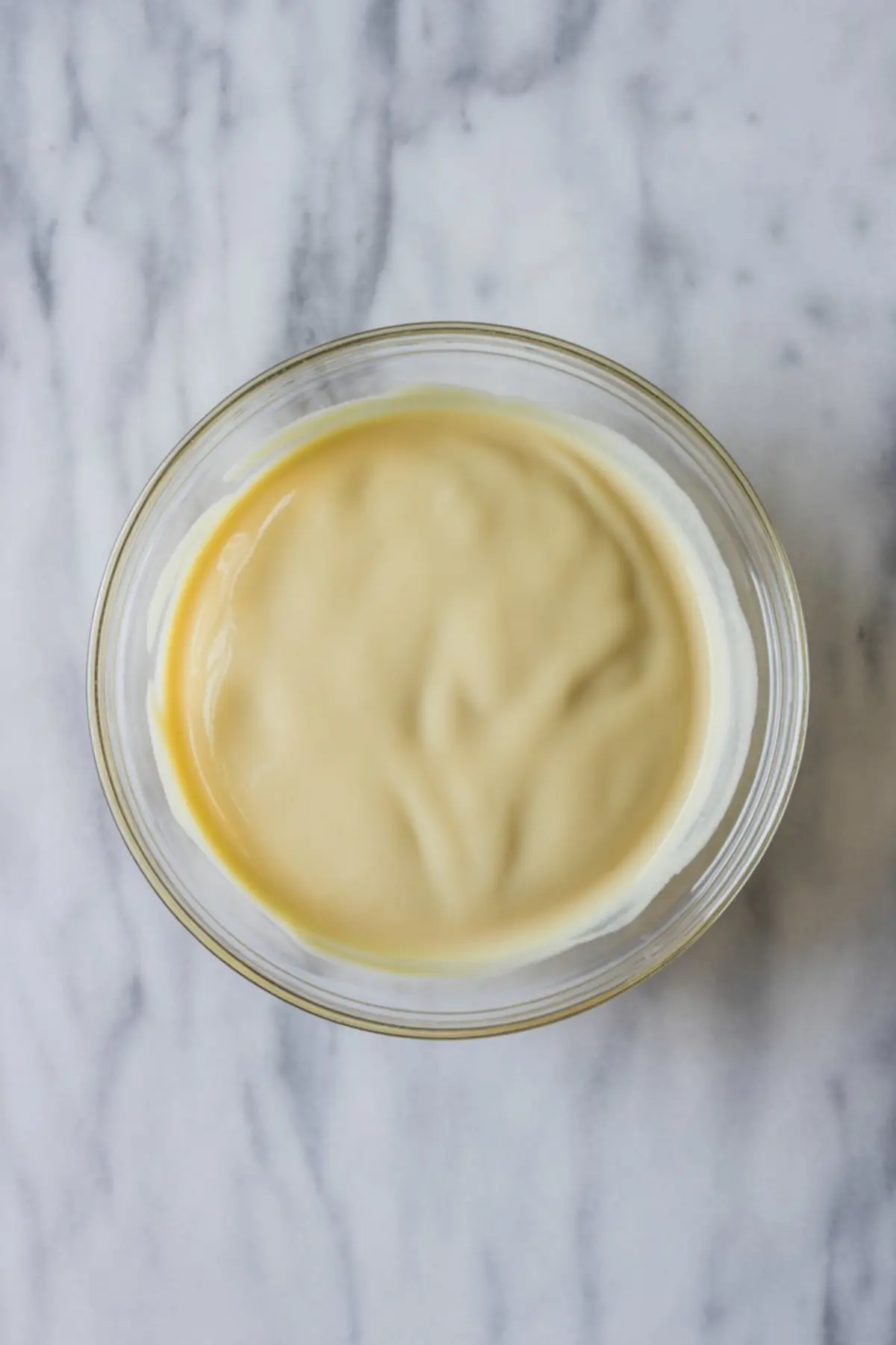 Creamy vanilla custard in a glass bowl on a marble surface, showcasing a smooth, rich texture ideal for desserts, fillings, or custard-based recipes.
