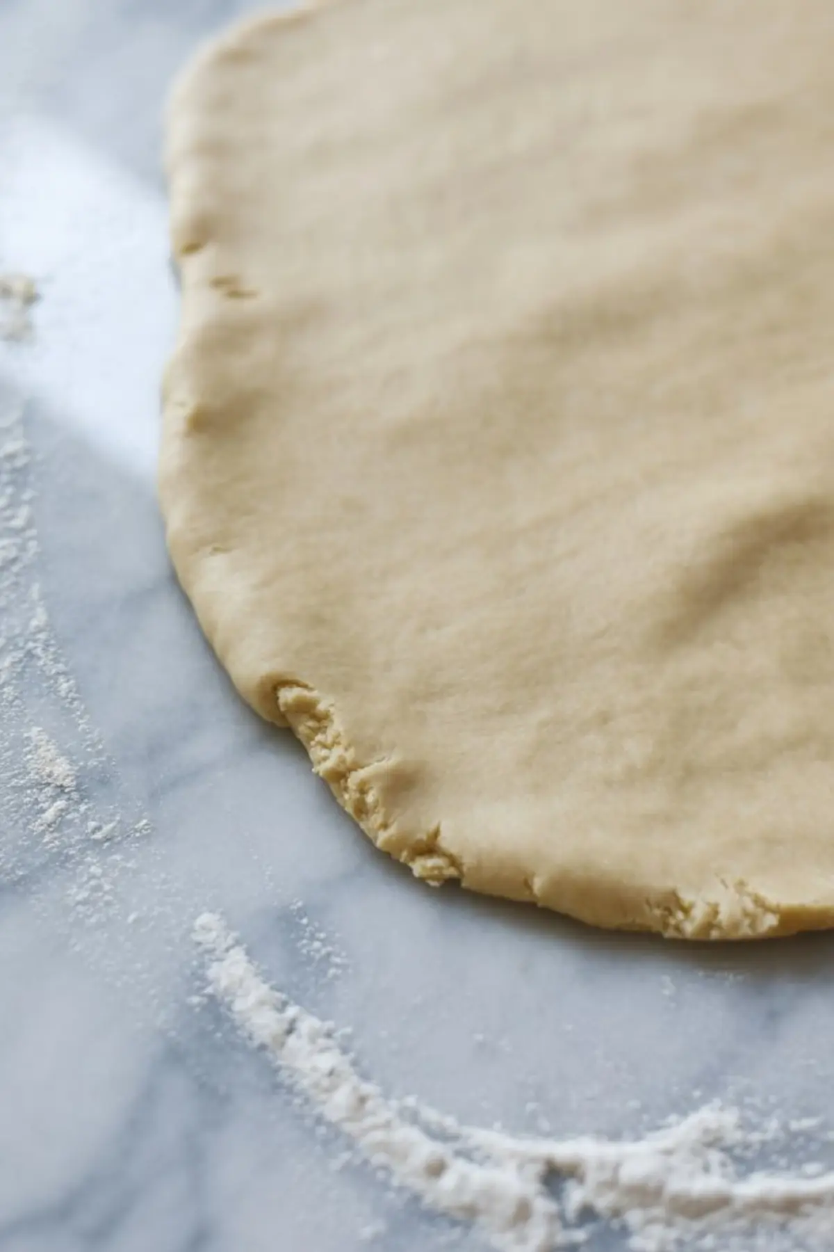 Rolled sugar cookie dough on a floured marble surface, ready for cutting into shapes for holiday baking.