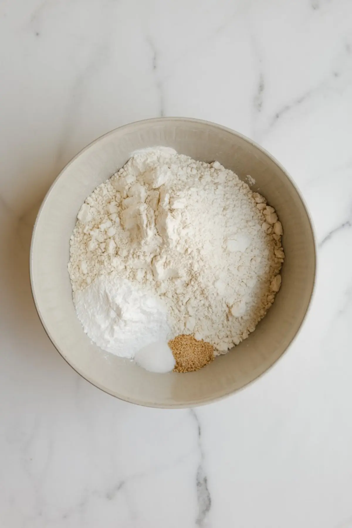 Dry ingredients in a mixing bowl, featuring flour, baking powder, baking soda, salt, and golden sanding sugar, ready for blending into cookie dough.
