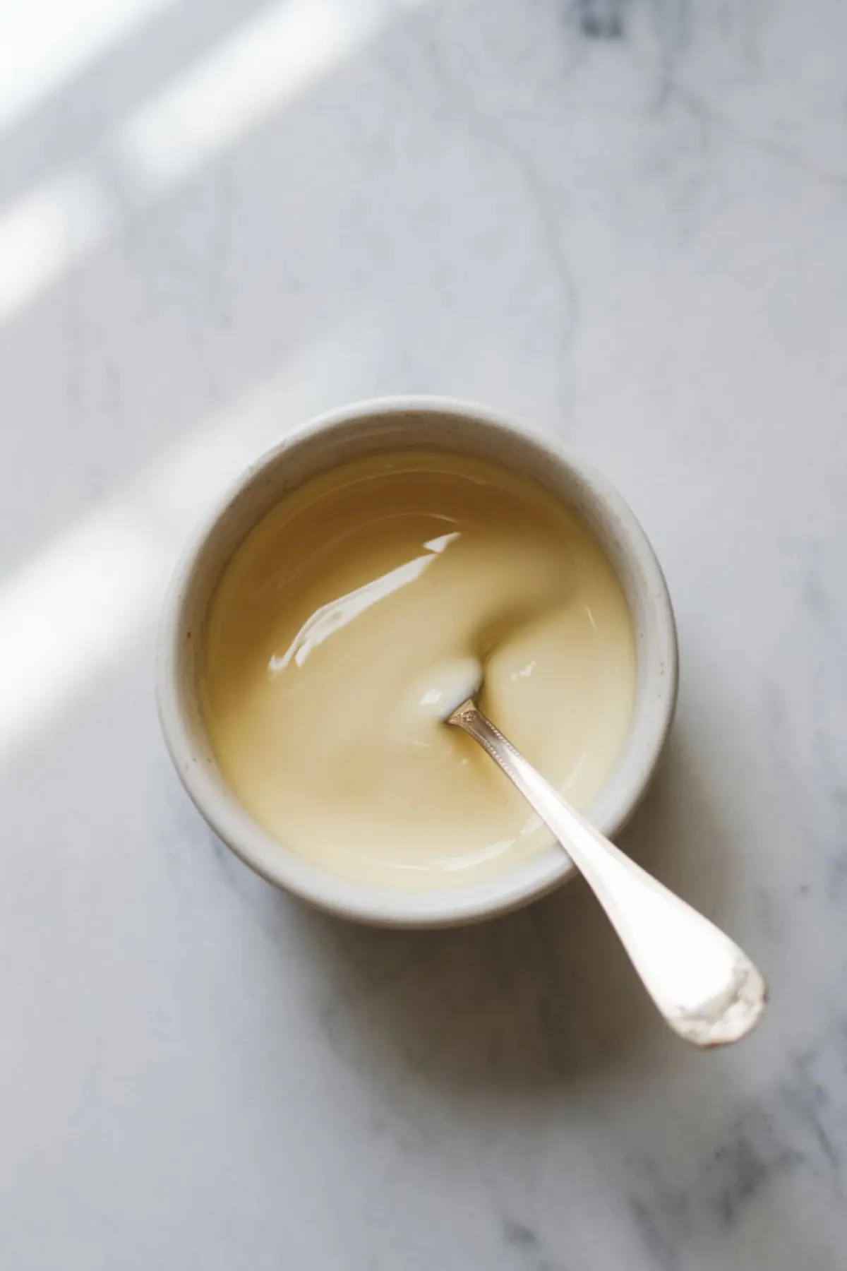 Glossy vanilla glaze in a small ceramic bowl with a silver spoon, perfect for icing cookies, cakes, or pastries.
