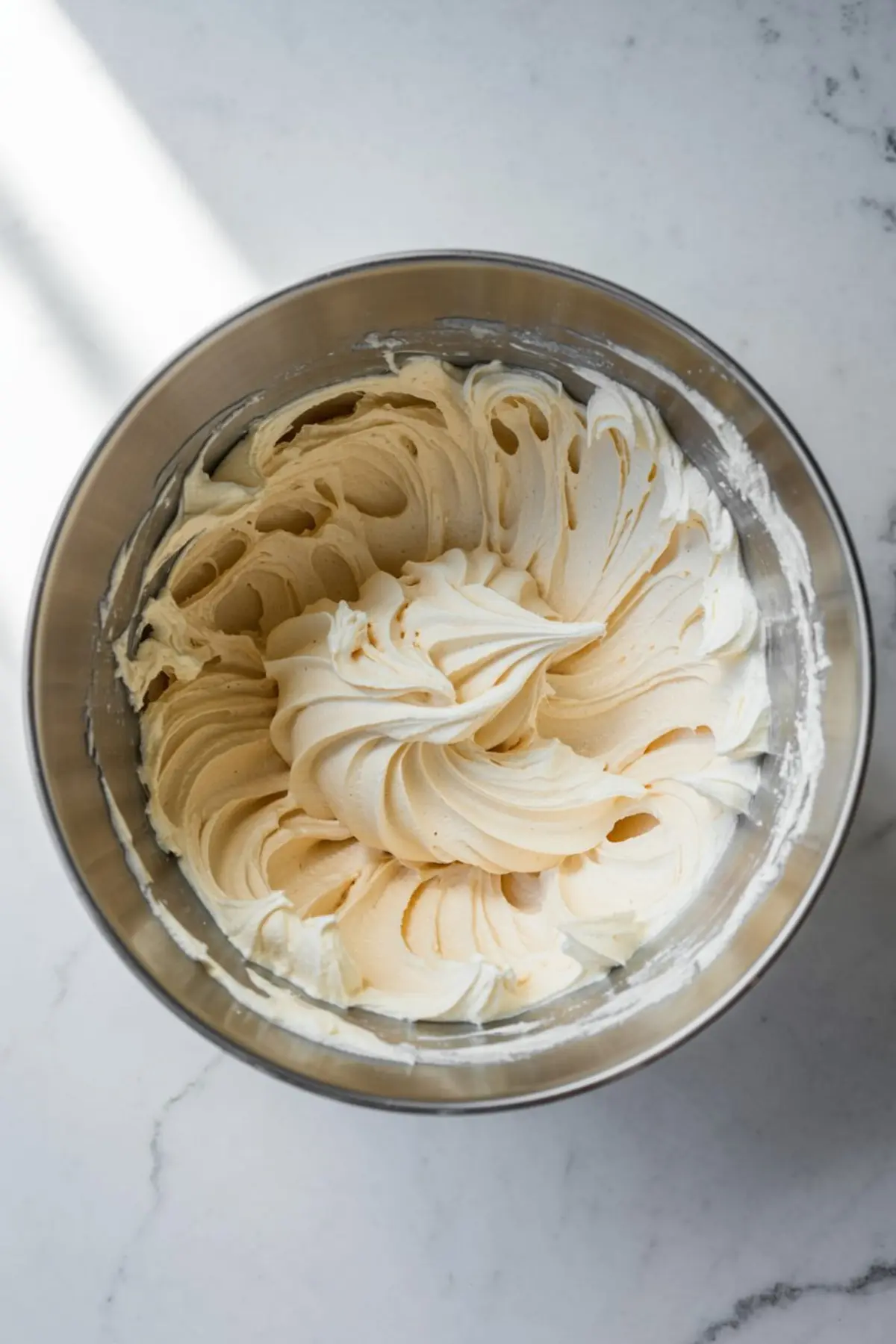 Smooth and fluffy cake batter whipped to stiff peaks in a stainless steel mixing bowl, photographed under natural light on a marble countertop.