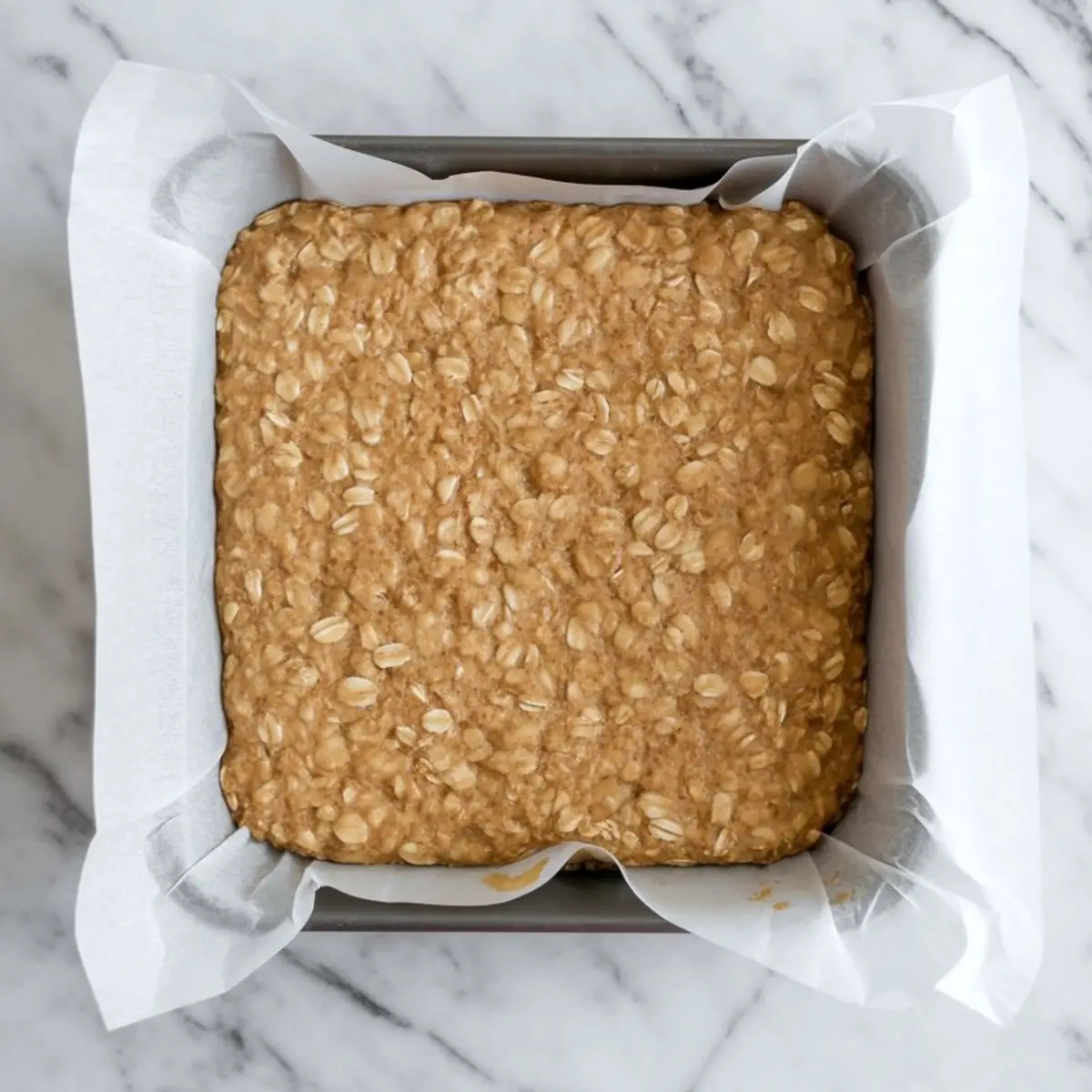 Baked oat crust pressed into a square baking dish lined with parchment paper, showing a golden, chewy texture with visible rolled oats.
