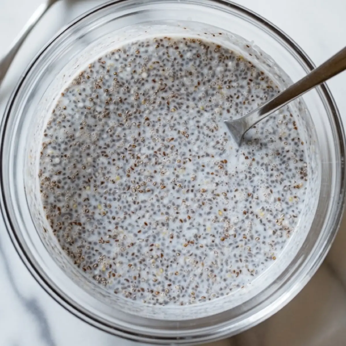 Stirred coconut chia pudding mixture with evenly soaked chia seeds in a glass container, ready for chilling.