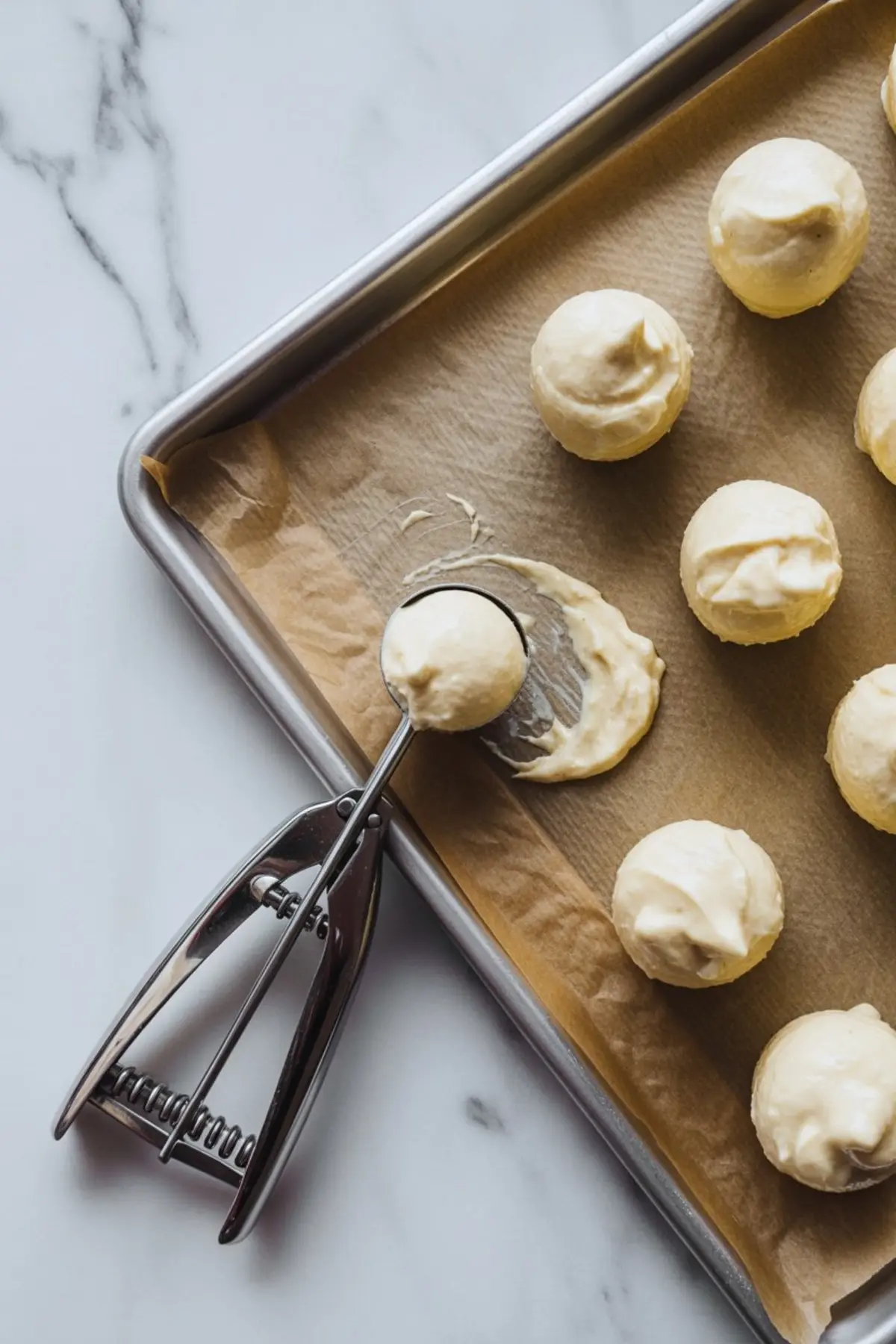 Parchment-lined baking sheet with round scoops of cream cheese dough, placed using a metal cookie scoop.