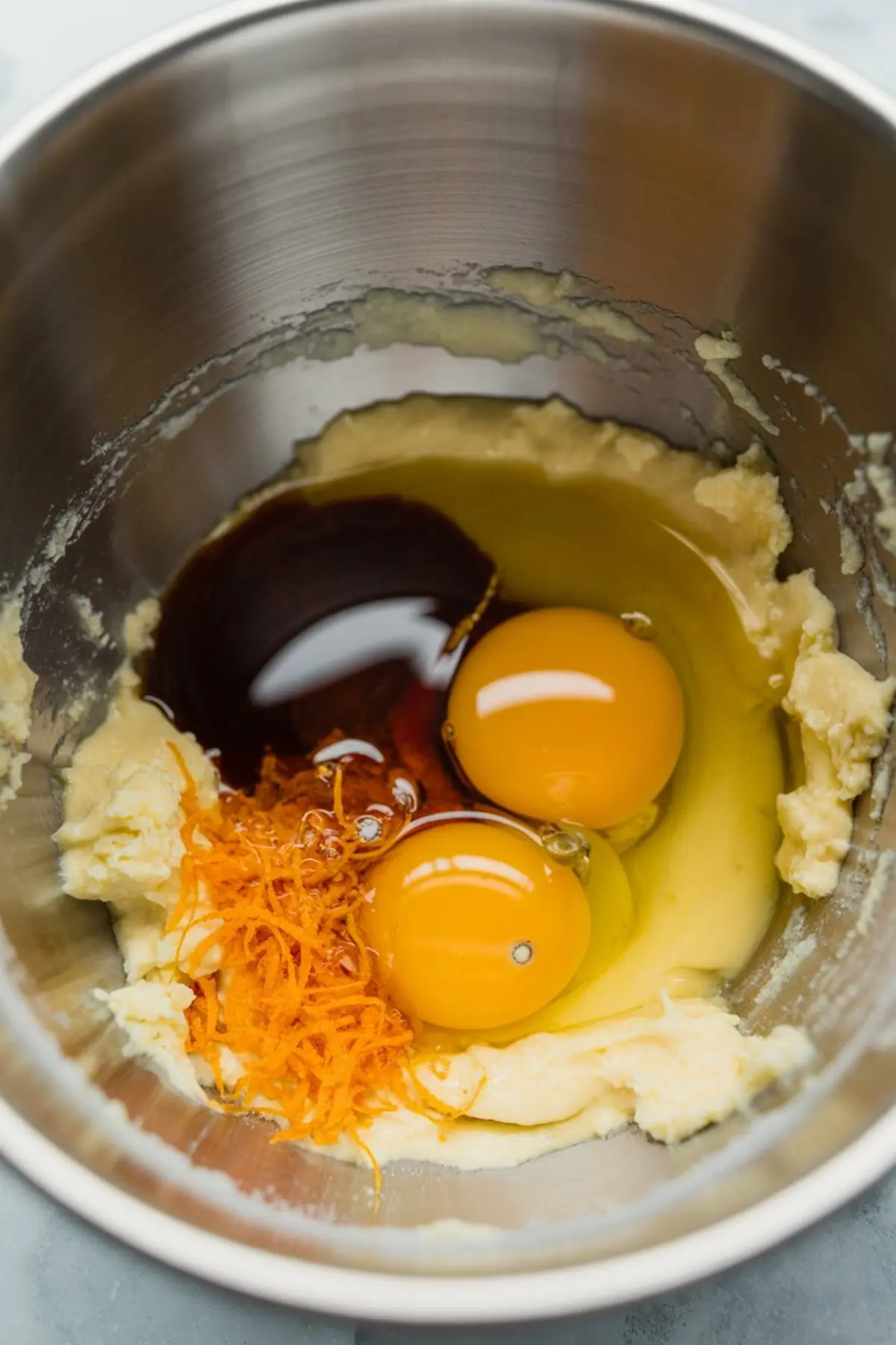 Stainless steel bowl with orange zest, vanilla extract, and cracked eggs added to creamed butter, capturing the flavor base for hazelnut orange cake.