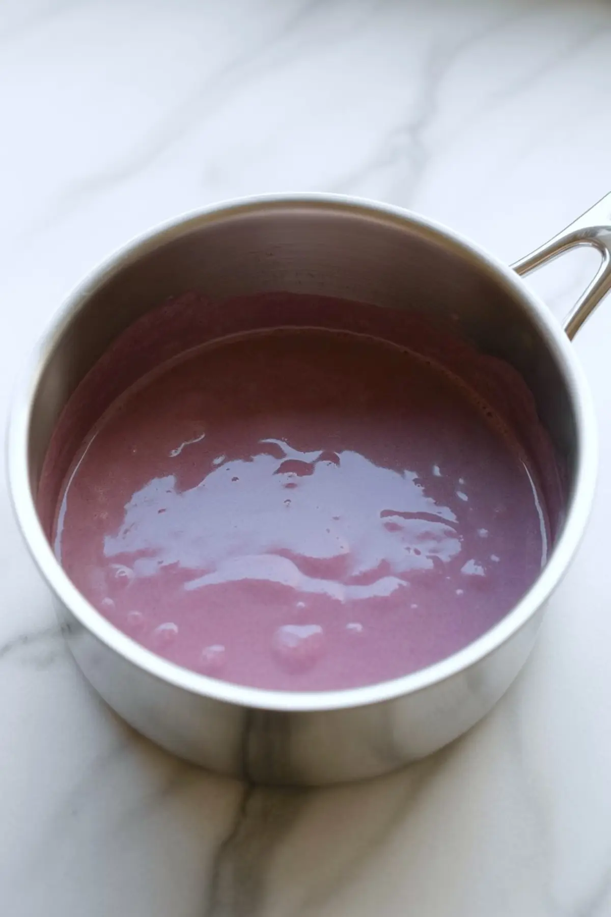 Smooth pink-purple panna cotta mixture in a saucepan, fully combined and ready for molding, with soft reflections on the surface.
