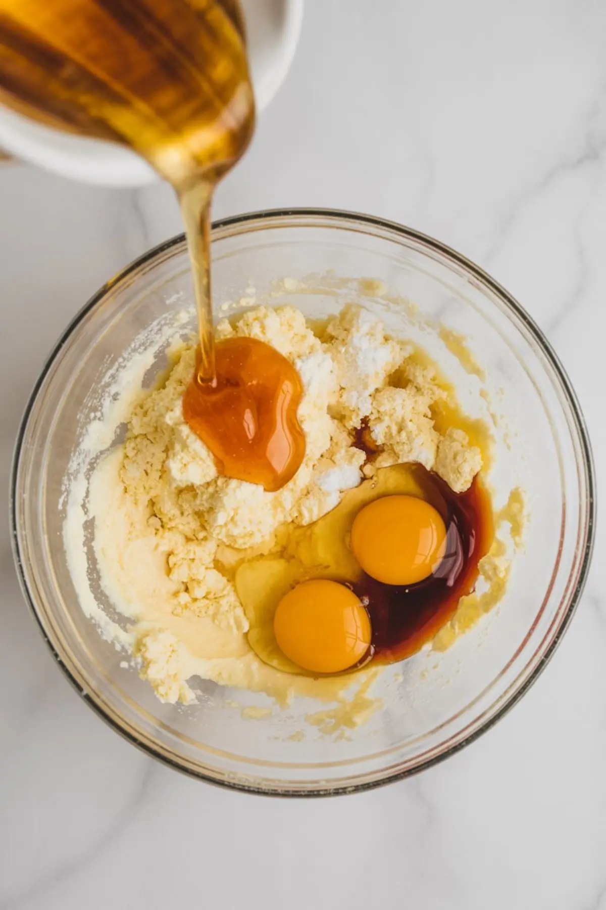 Honey pours into a mixing bowl with eggs, vanilla, and creamed butter mixture, captured from overhead to show glossy honey flowing into cookie dough ingredients.