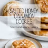 Salted honey cinnamon cookies rest on parchment paper with thick honey icing and flaky sea salt, shown close up to highlight cracked cookie edges and smooth glaze texture.