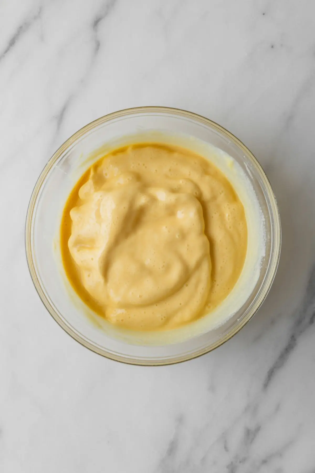 Smooth, thick honey custard mixture in a glass bowl on a white marble surface, freshly mixed and ready to be poured into a pie crust for baking.
