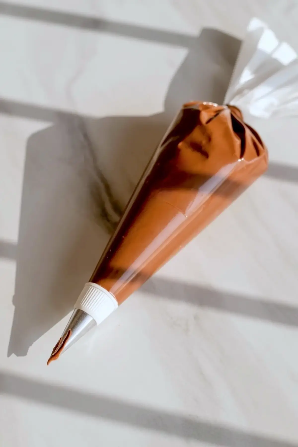 Chocolate pastry cream fills a piping bag with metal tip, shown close up on a marble surface, ready for filling bomboloni donuts.