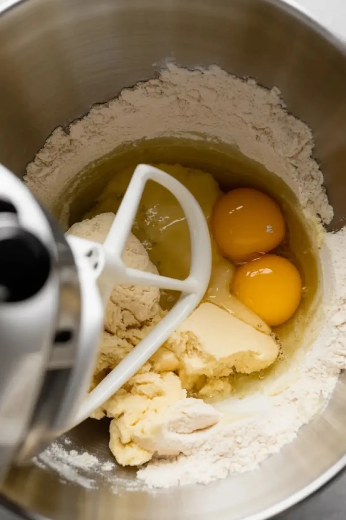 Bomboloni dough ingredients mix in a stand mixer bowl with flour, eggs, butter, and sugar, captured before kneading begins.