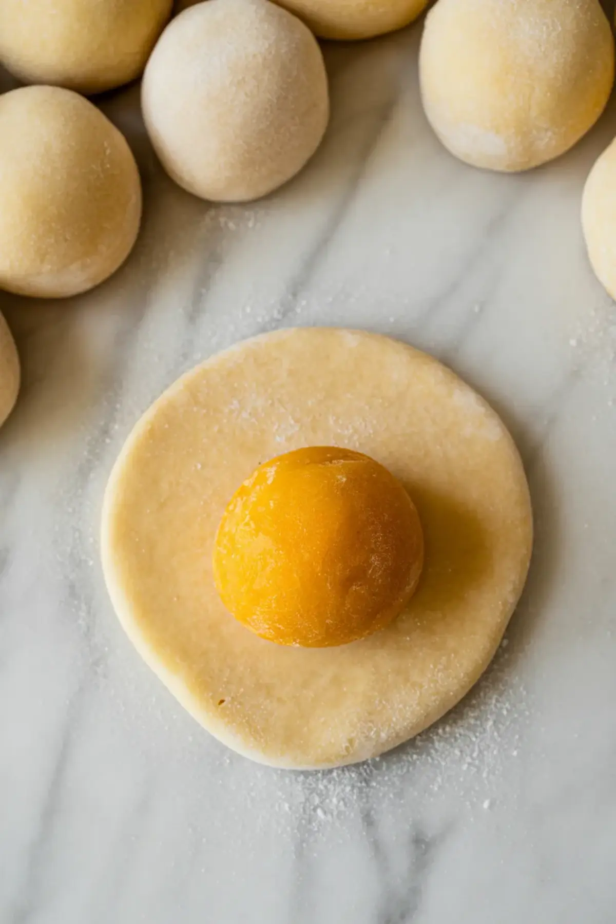 Square portions of mochi dough dusted with starch sit on parchment paper beside a metal dough scraper, showing mango mochi dough shaping.