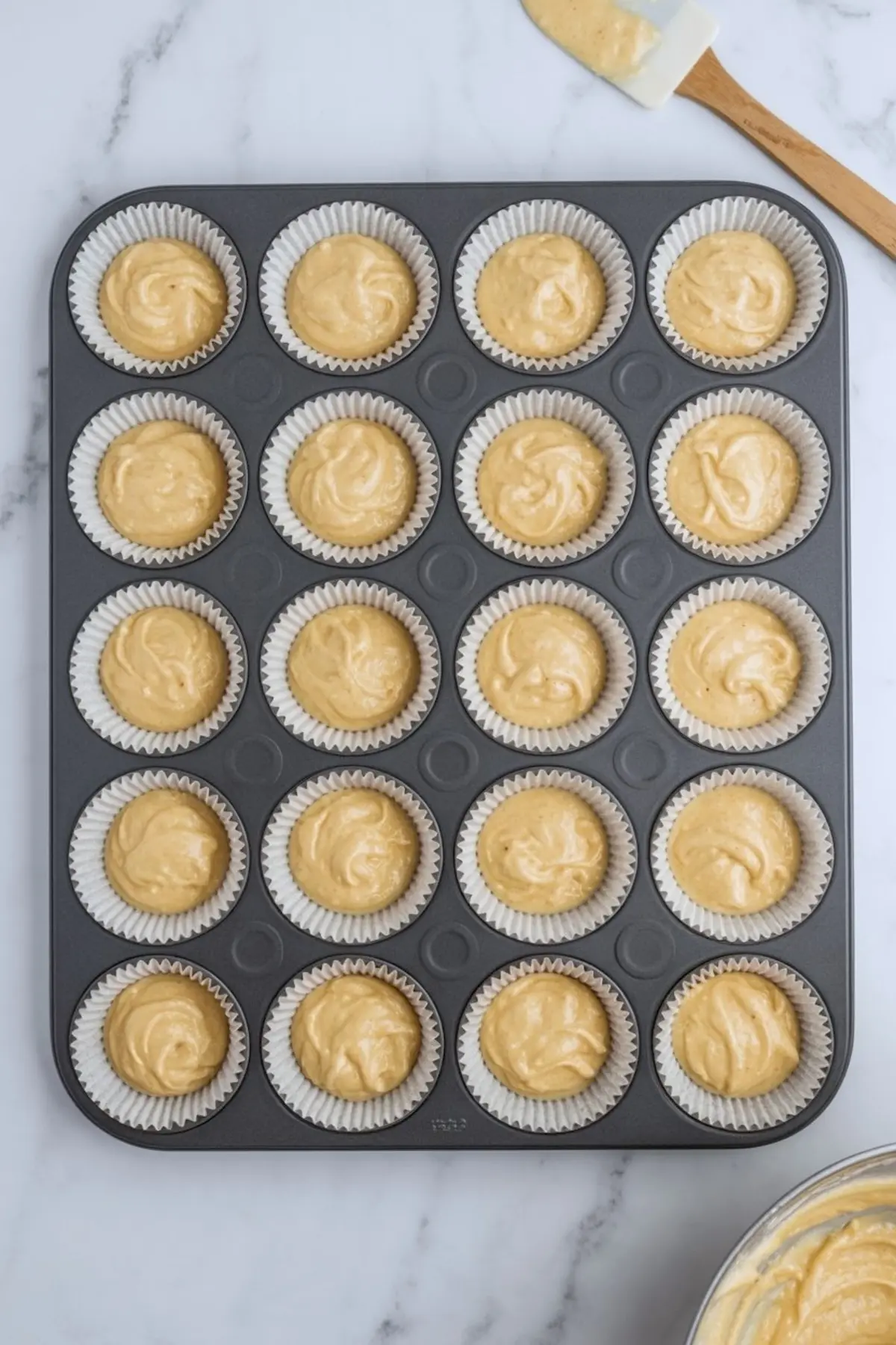 Cupcake tray filled with raw vanilla batter in paper liners, arranged neatly before baking on a marble countertop during dessert preparation.
