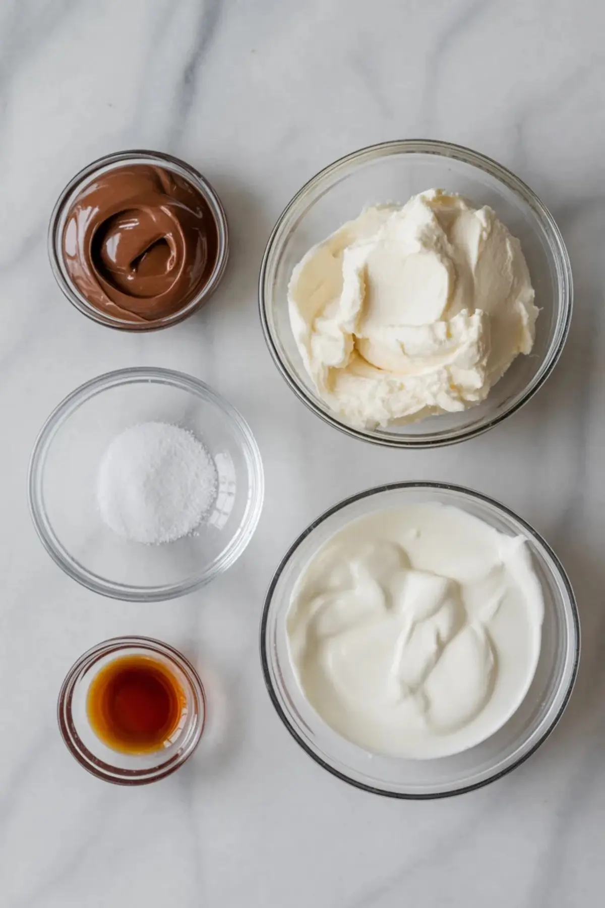 Glass bowls on a marble surface filled with Nutella, mascarpone cheese, Greek yogurt, granulated sugar, vanilla extract, and whipped cream.
