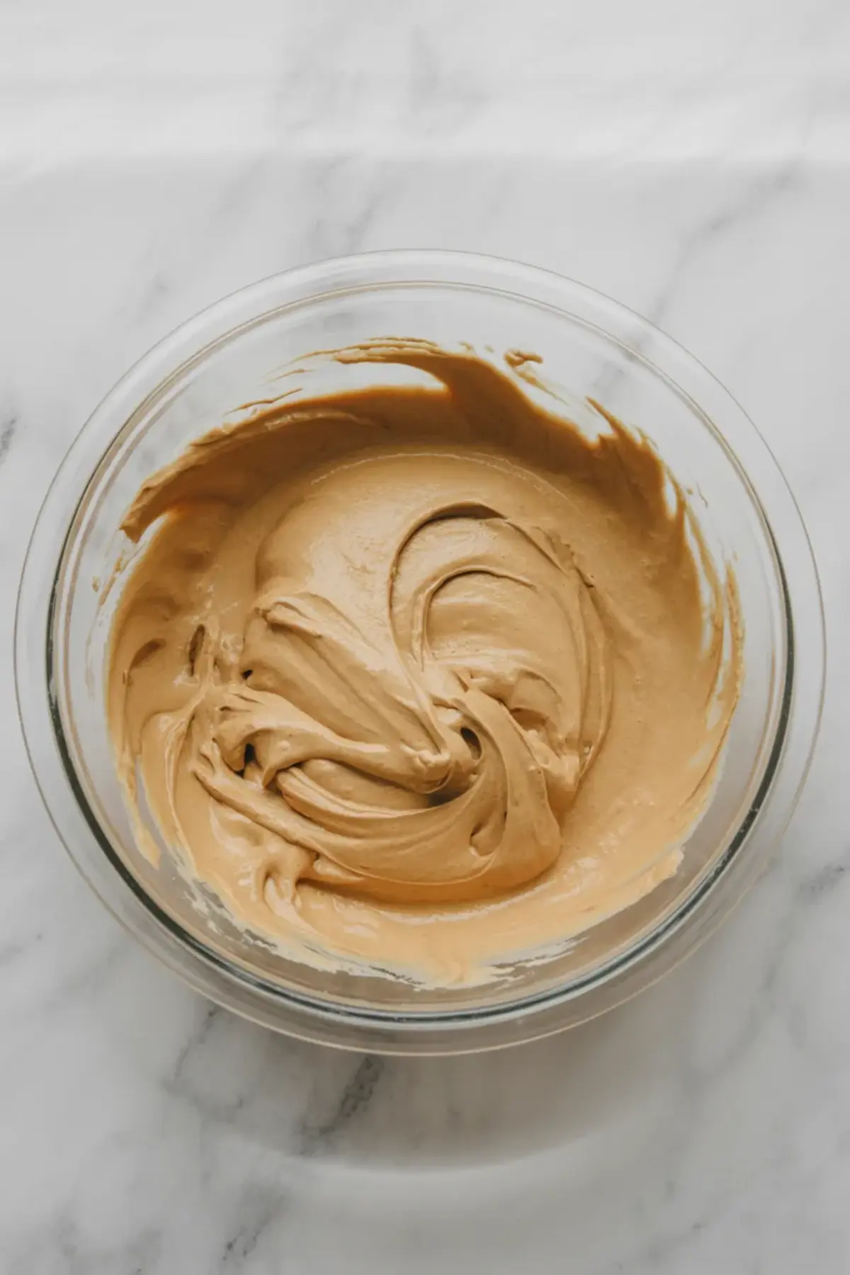 Fully mixed peanut butter mousse in a glass bowl with swirled texture, sitting on a marble countertop.