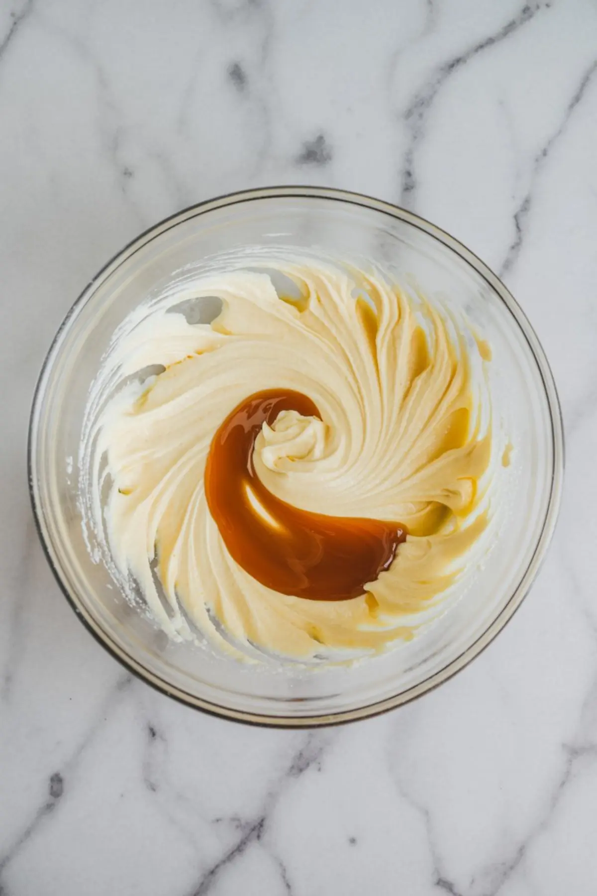 Bowl of whipped buttercream frosting with a swirl of vanilla extract on top, highlighting the mixing process for Russian buttercream made with sweetened condensed milk.