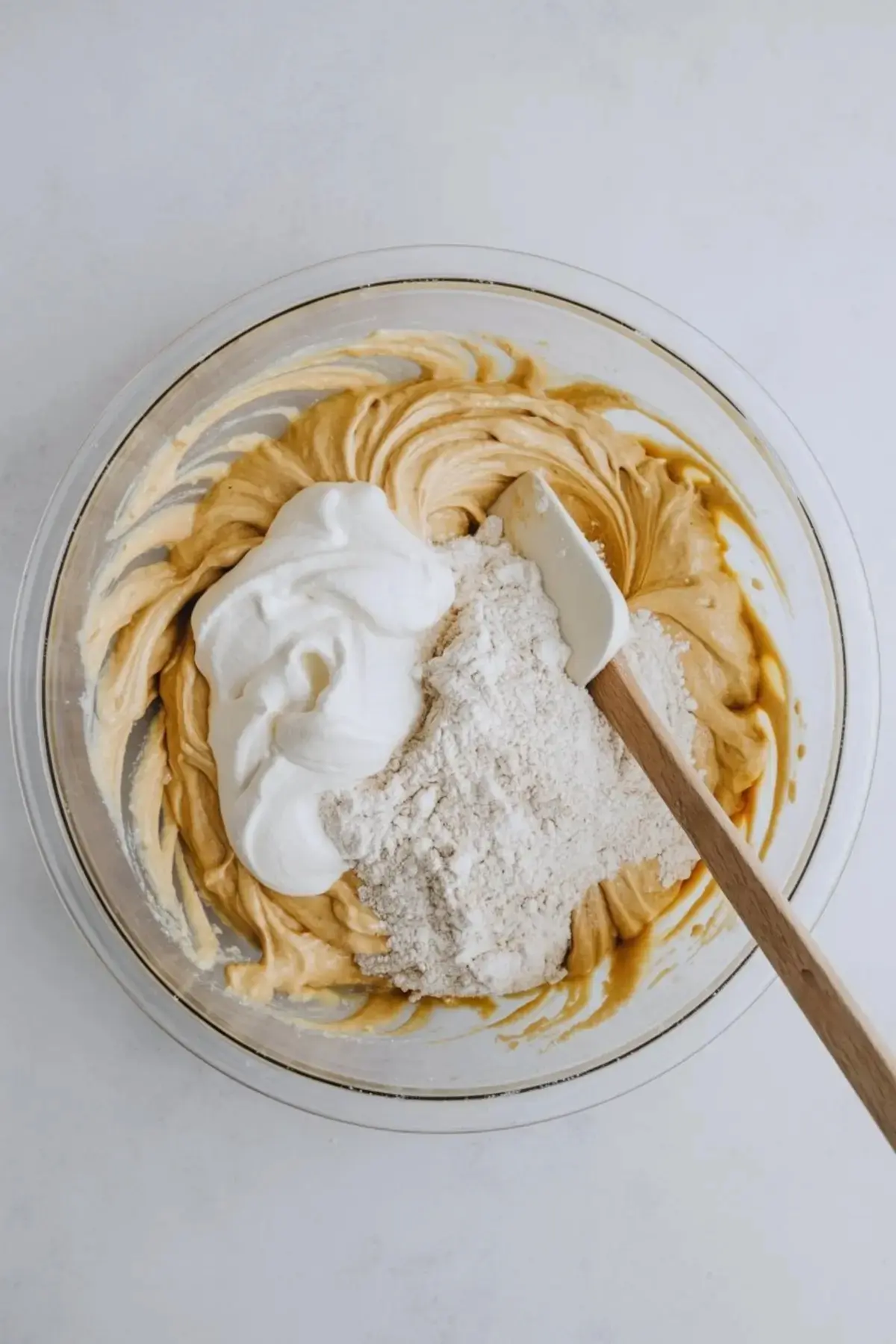 Bowl of partially mixed cake batter with whipped egg whites and dry flour mixture sitting on top, with a spatula resting on the edge.
