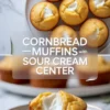 Metal muffin tin holds paper liners filled with cornbread batter on a marble countertop. Glass bowl of batter and measuring scoop sit beside the pan, showing step by step cornbread muffin preparation.