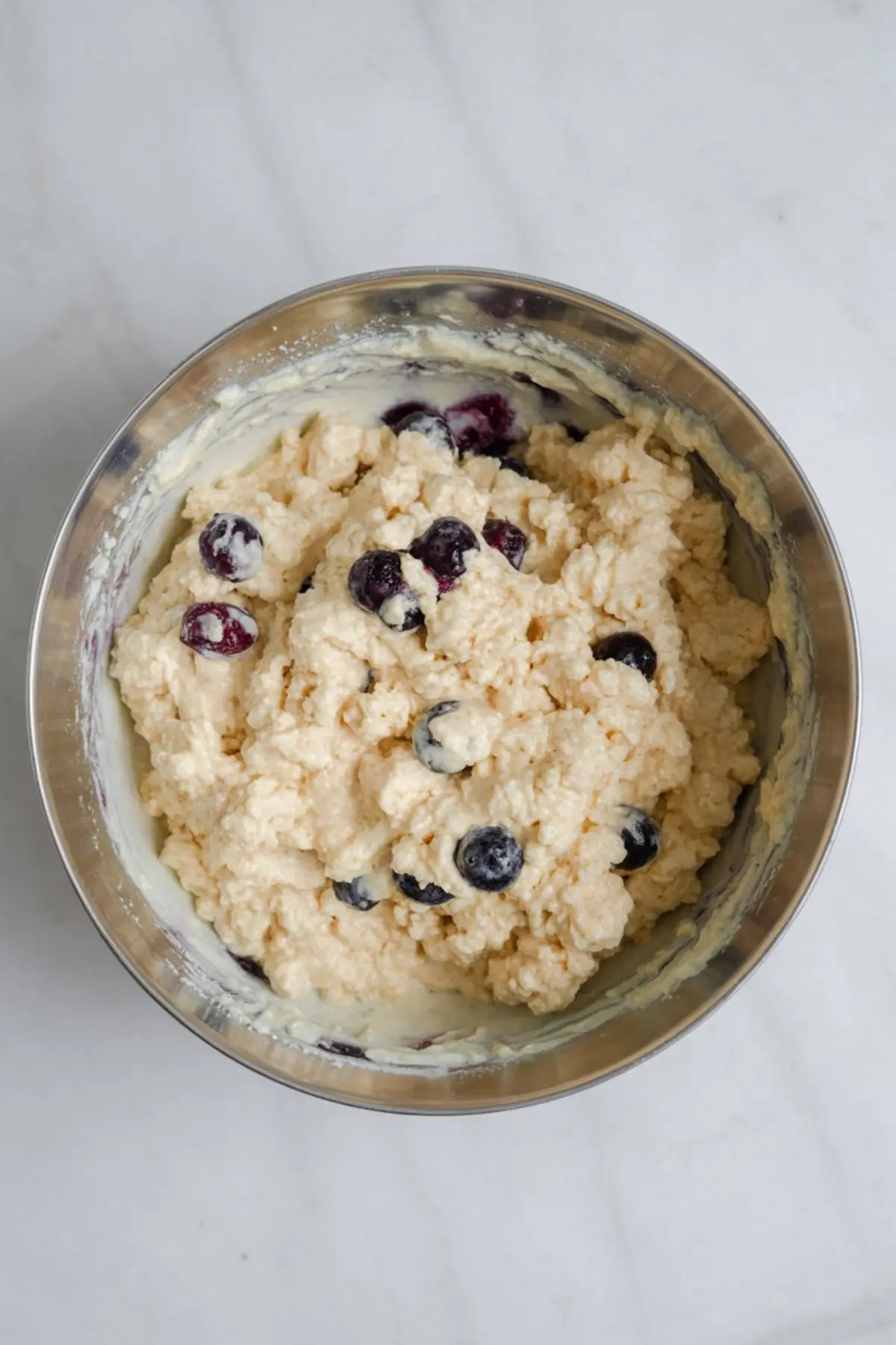 Thick blueberry pancake batter in a metal bowl, featuring visible cottage cheese curds and fresh blueberries, ready for cooking.
