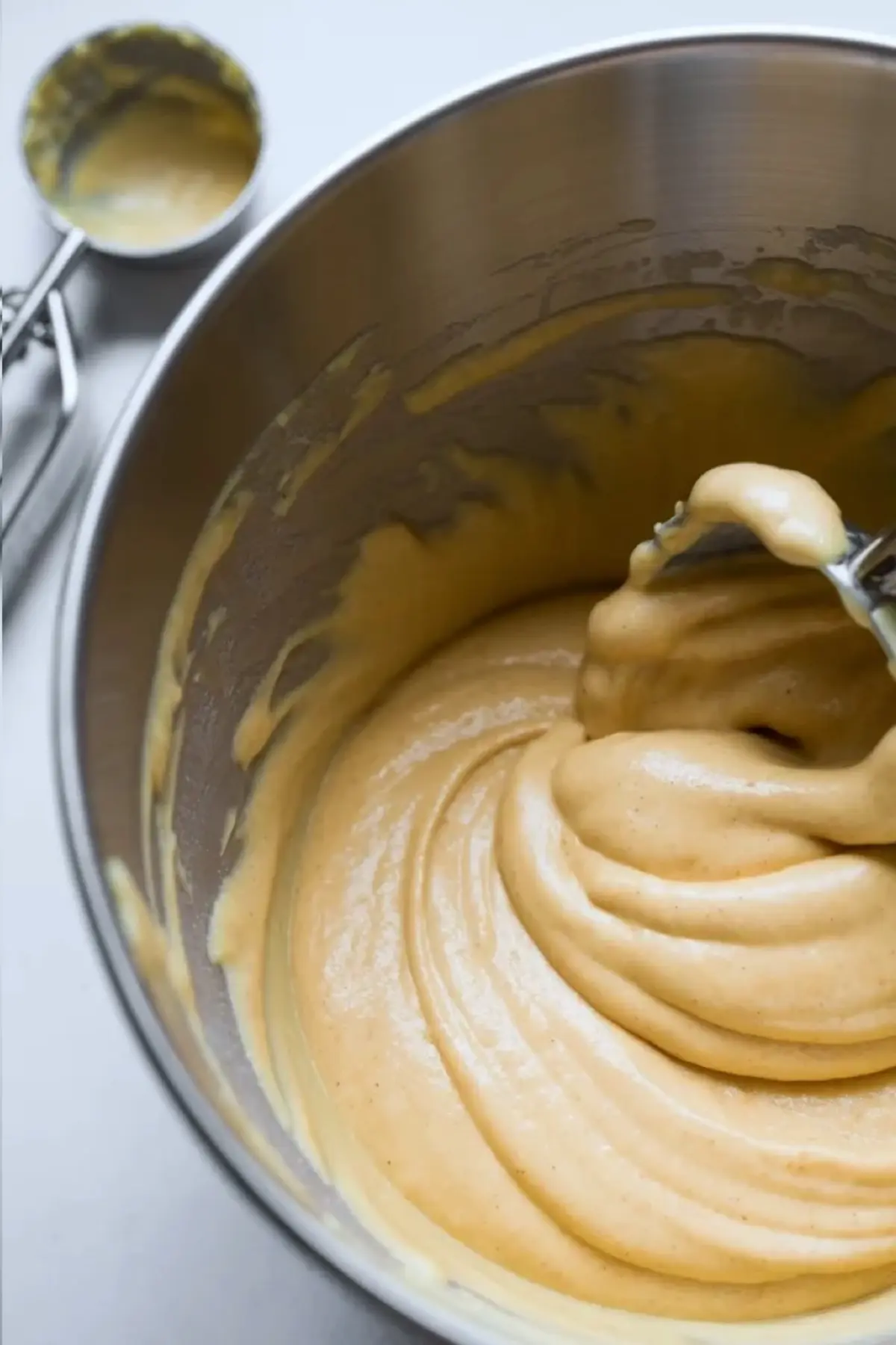 Smooth cupcake batter with a creamy texture inside a stainless steel mixing bowl, with a cookie scoop resting nearby on a light background.
