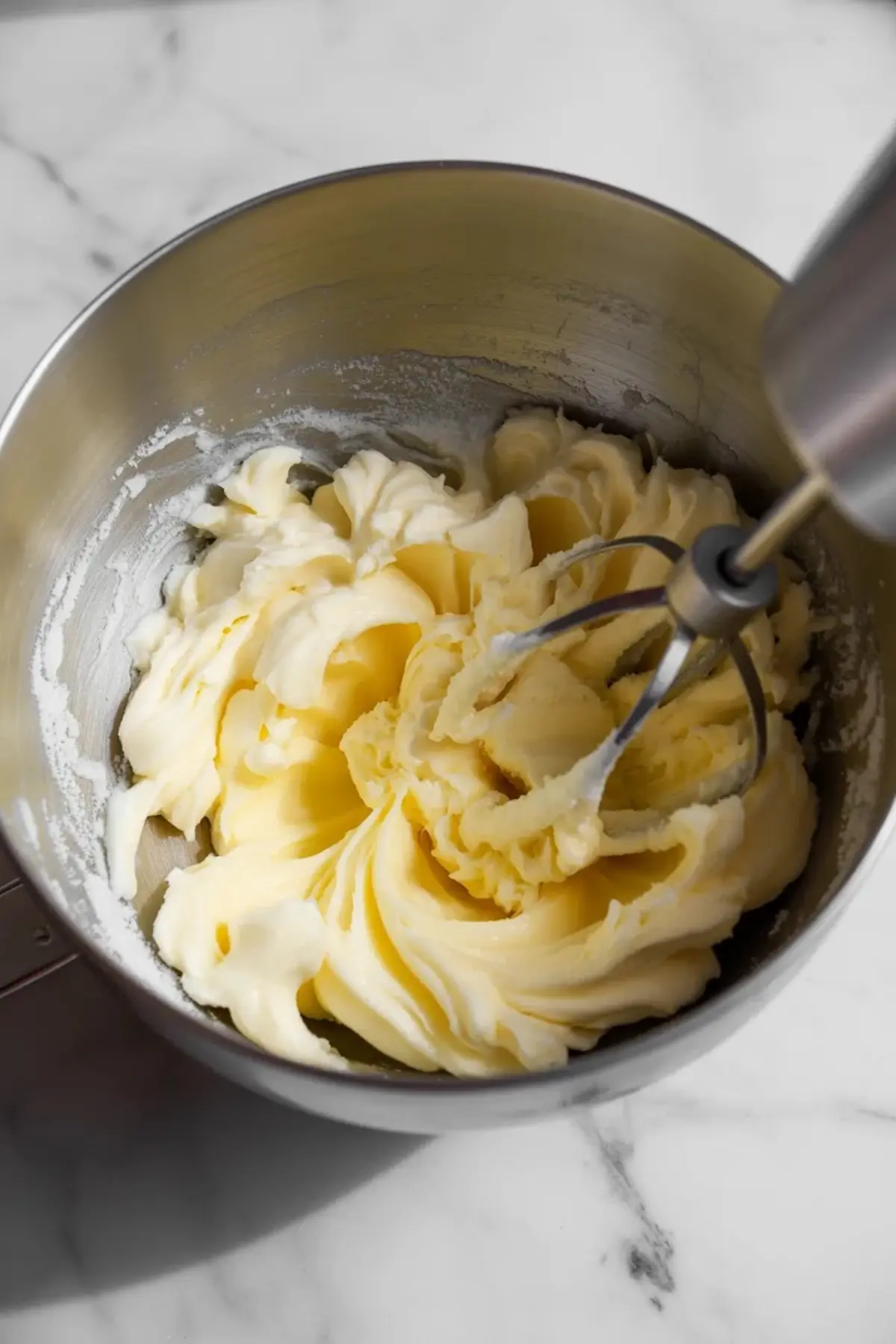 Creamed butter and sugar mixture whipped to a light texture inside a stainless steel bowl using a handheld electric mixer.
