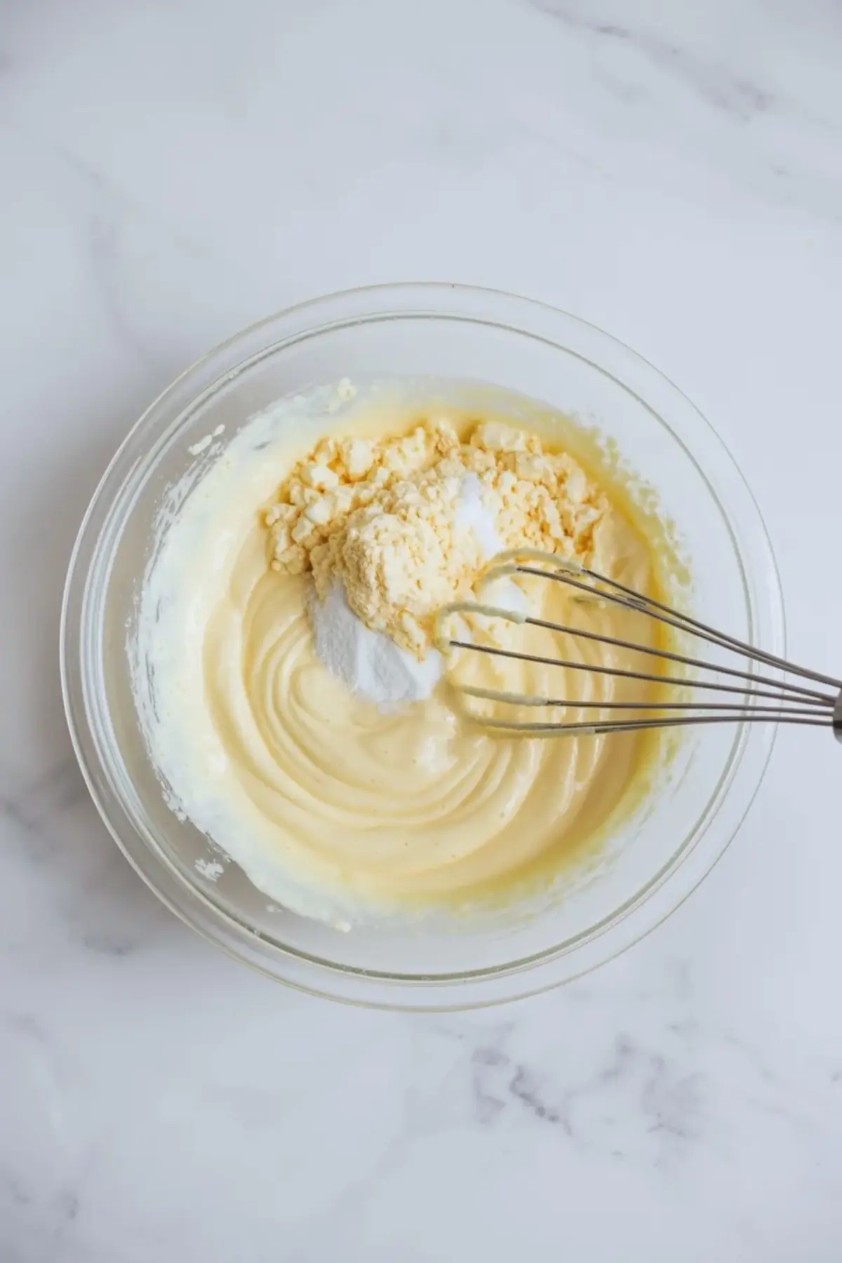 Metal whisk mixes vanilla pudding and powdered mix in a glass bowl, creating a smooth and creamy custard base for easy no bake banana pudding dessert.
