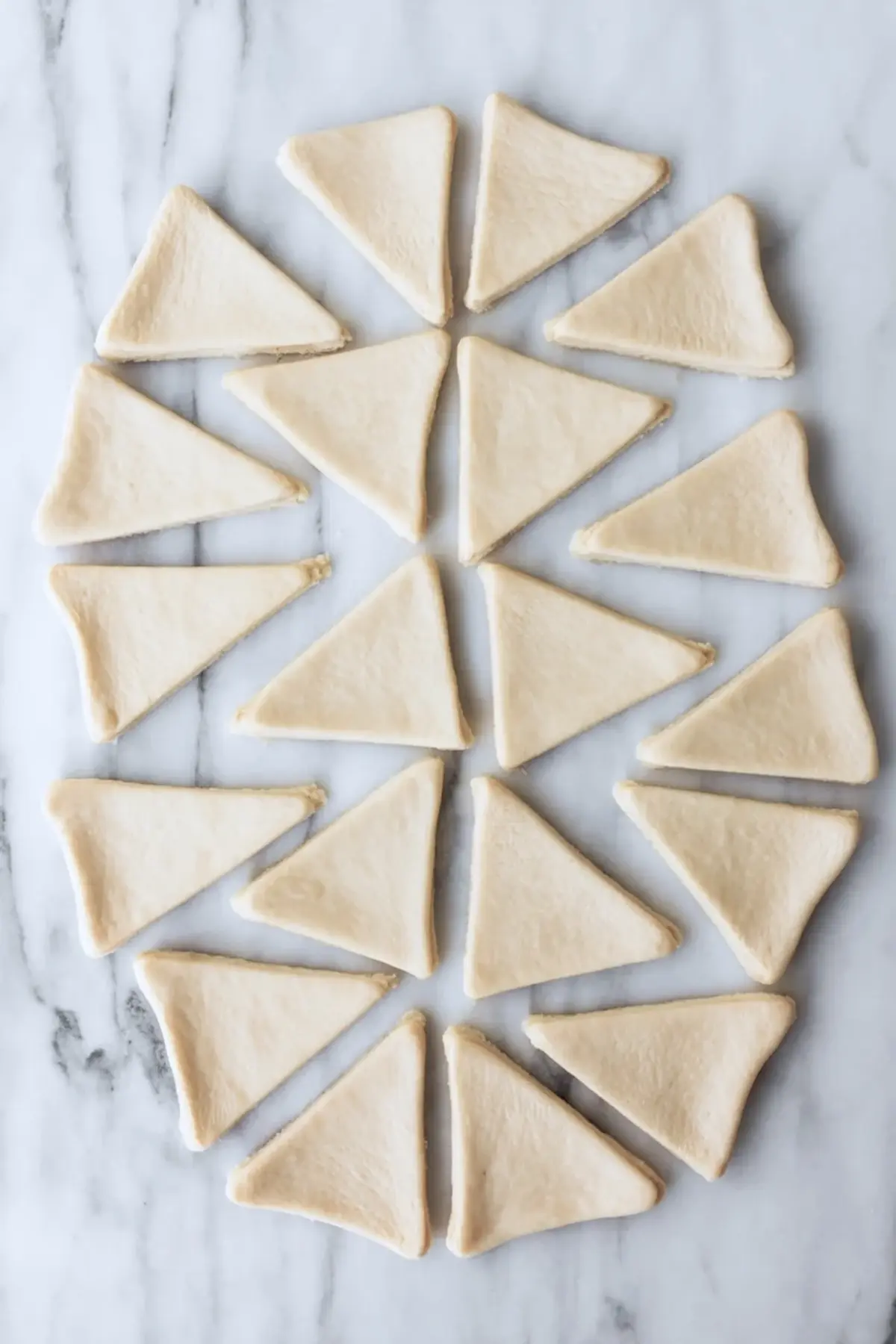 Unbaked crescent dough triangles arranged in a circular pattern on a marble surface, prepared for shaping into Easter bunny crescent rolls.
