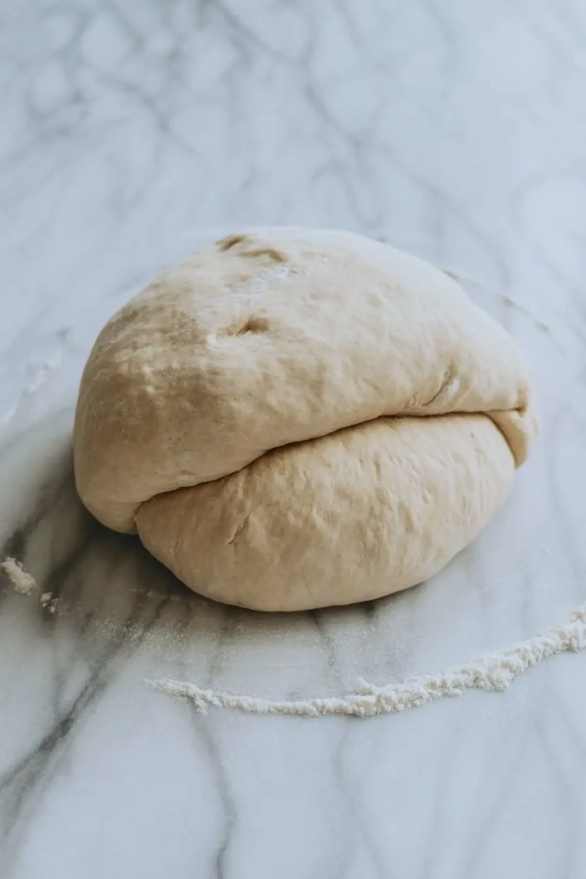 Ball of homemade bread dough rests on a lightly floured marble surface. Dough shows a smooth elastic texture ready for proofing in a sweet Italian Easter bread recipe.