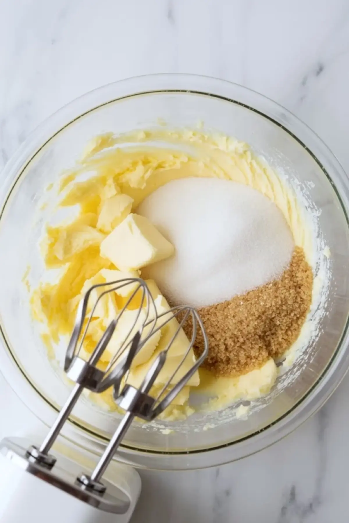 Glass mixing bowl contains softened butter, granulated sugar, and brown sugar with electric mixer beaters inside. Creamed butter and sugar mixture forms the base for chewy espresso crinkle cookies.