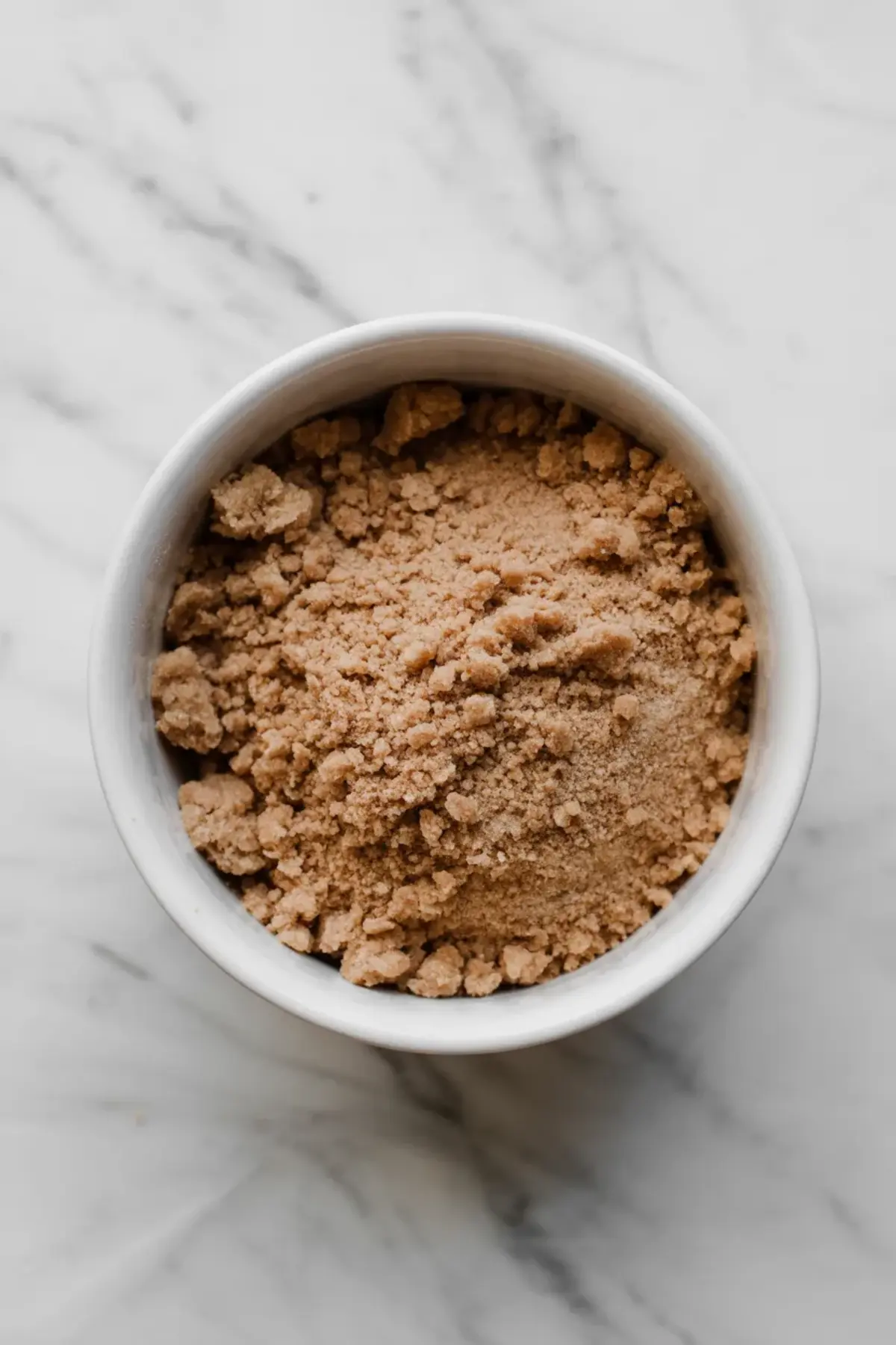 Small white bowl holds crumbly cinnamon streusel topping made with gluten free flour, brown sugar, and butter. The image shows streusel texture for homemade gluten free coffee cake and bakery style crumb topping.