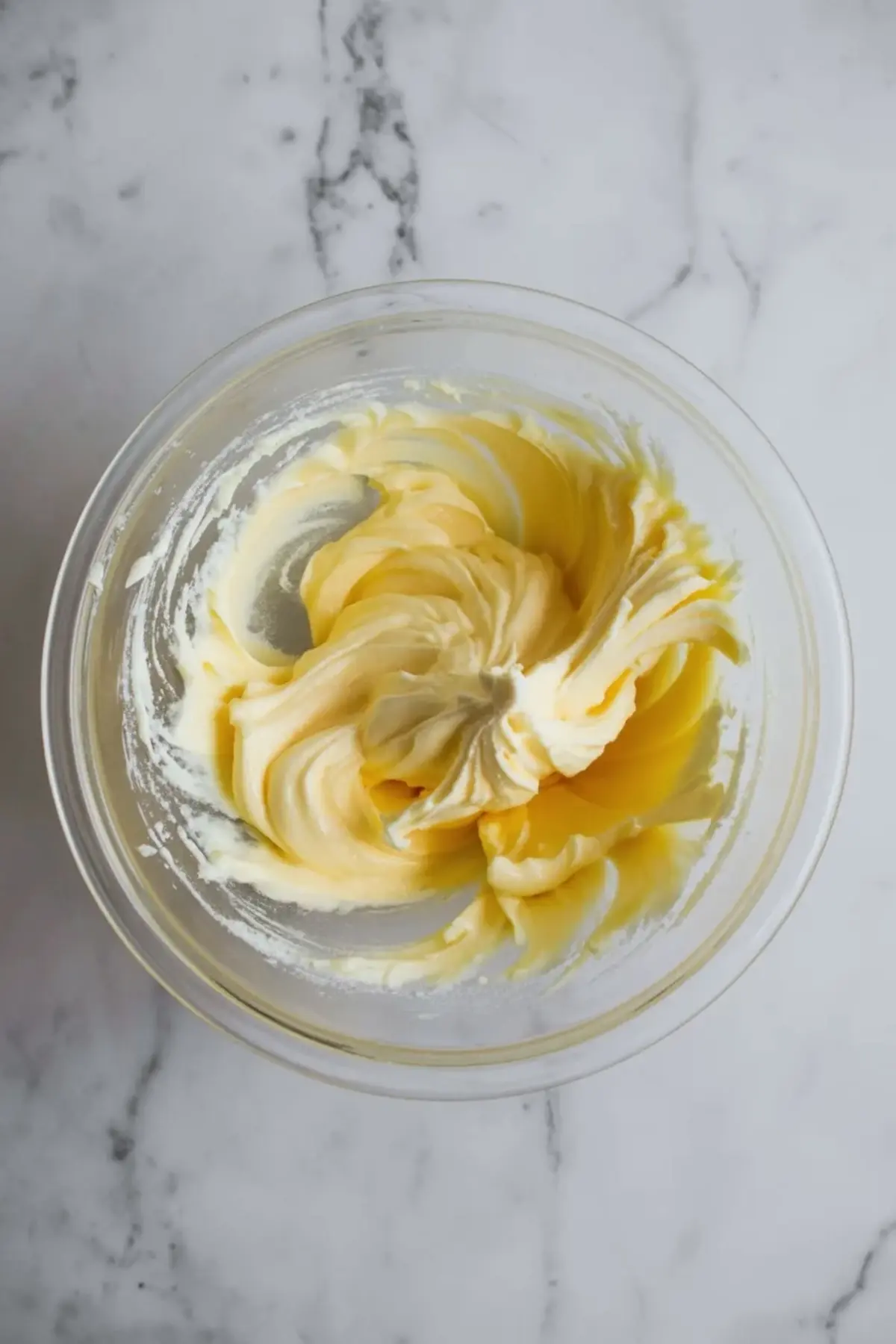 Creamed butter and sugar mixture whipped to a light and fluffy texture in a glass mixing bowl, showing the essential base for butter cookies or cakes.