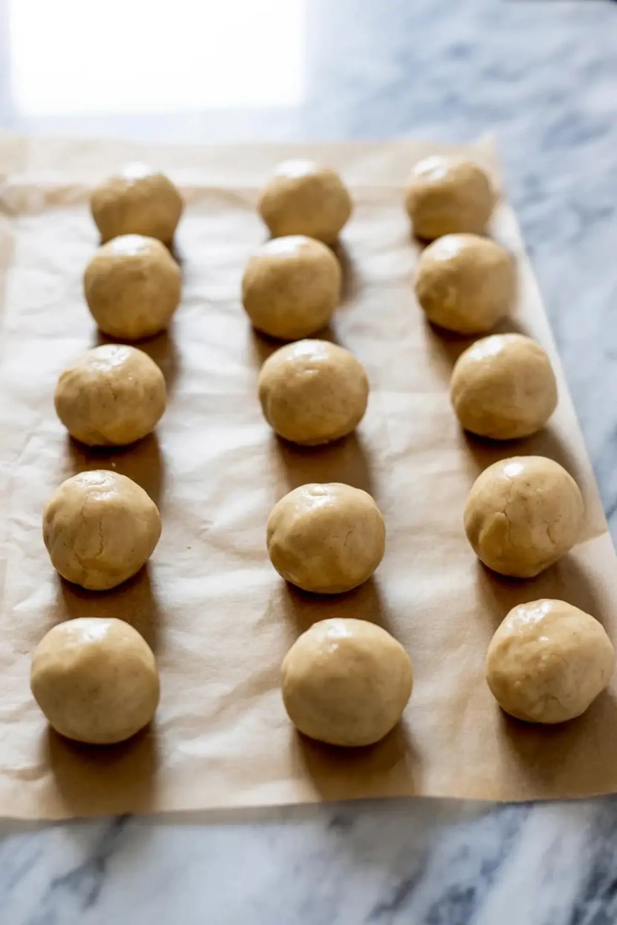 Round cookie dough balls line a parchment paper baking sheet, evenly spaced and ready for baking classic thumbprint cookies.
