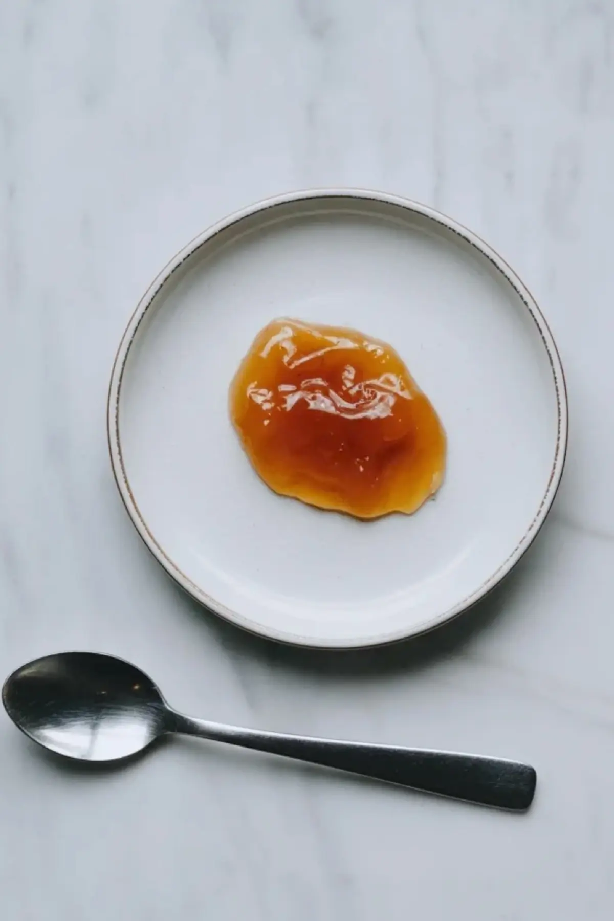 A spoonful of apricot jam sits on a white plate beside a spoon to show the jam texture.