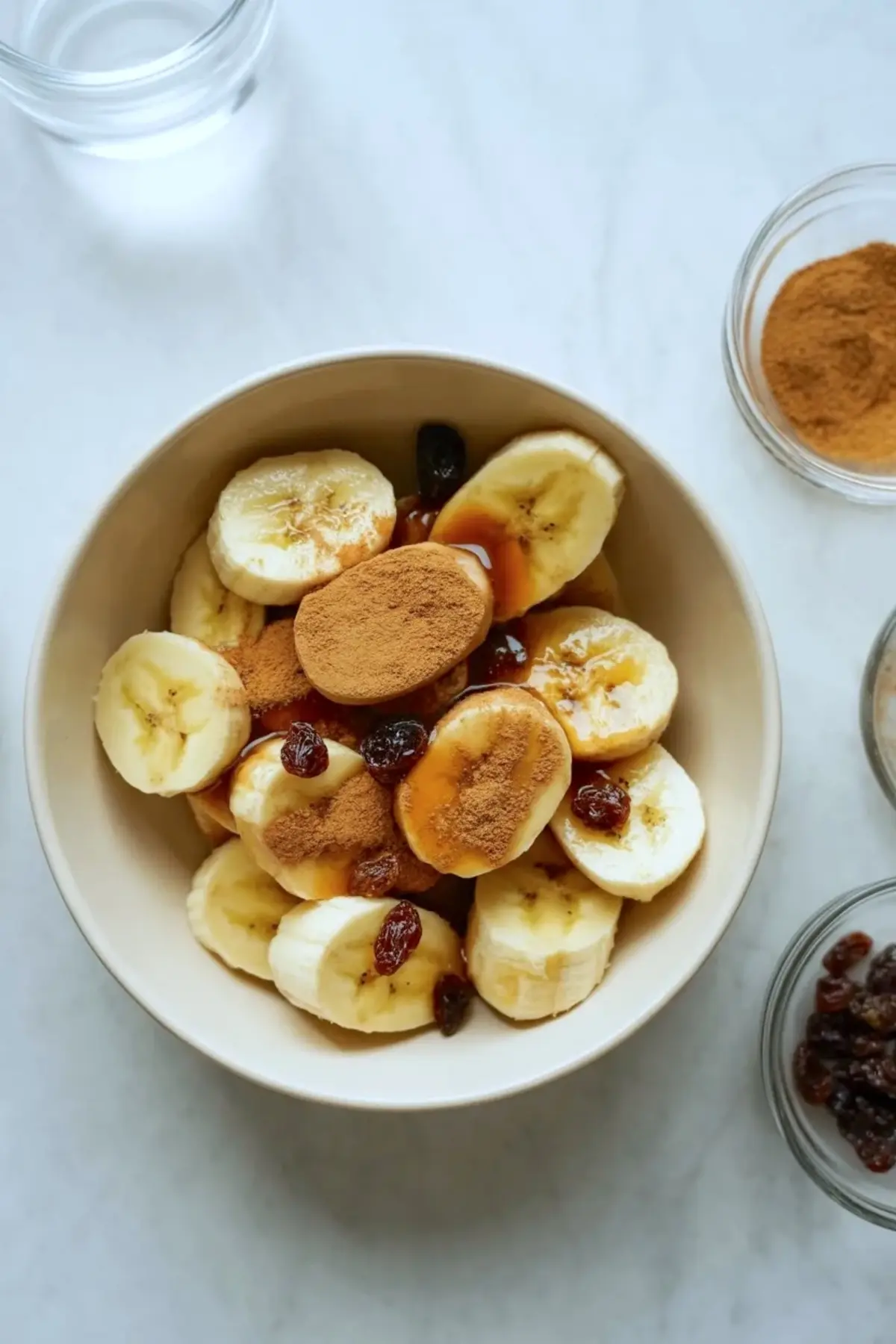 Banana strudel filling in a bowl with sliced bananas, cinnamon, raisins, and syrup before it is wrapped in phyllo.