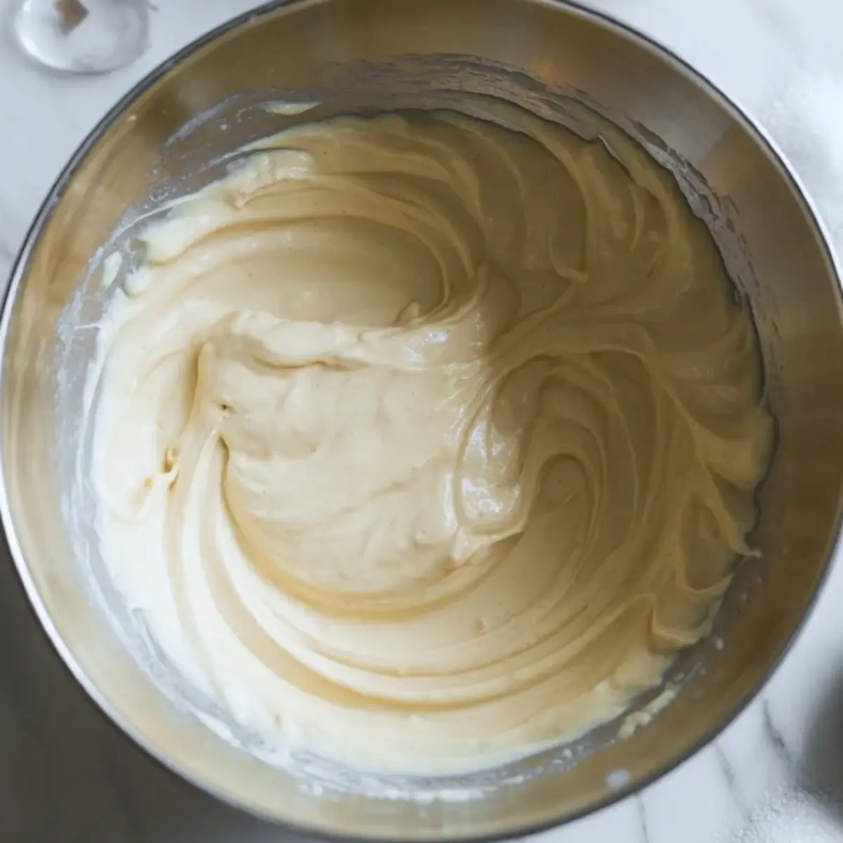 Smooth cheesecake filling in a metal mixing bowl for blueberry cheesecake crumb bars before it is spread into the pan.