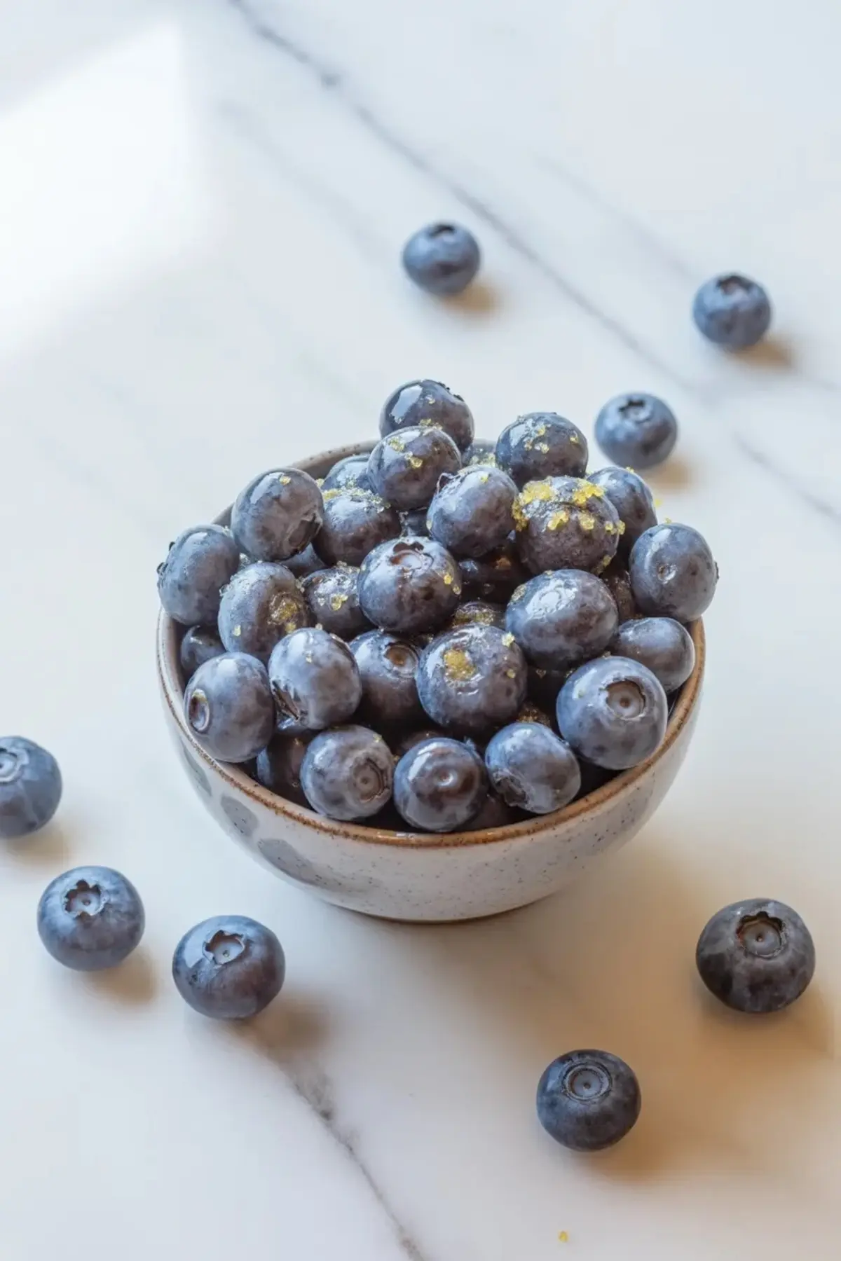 Fresh blueberries piled in a small bowl on white marble for blueberry cheesecake crumb bars.