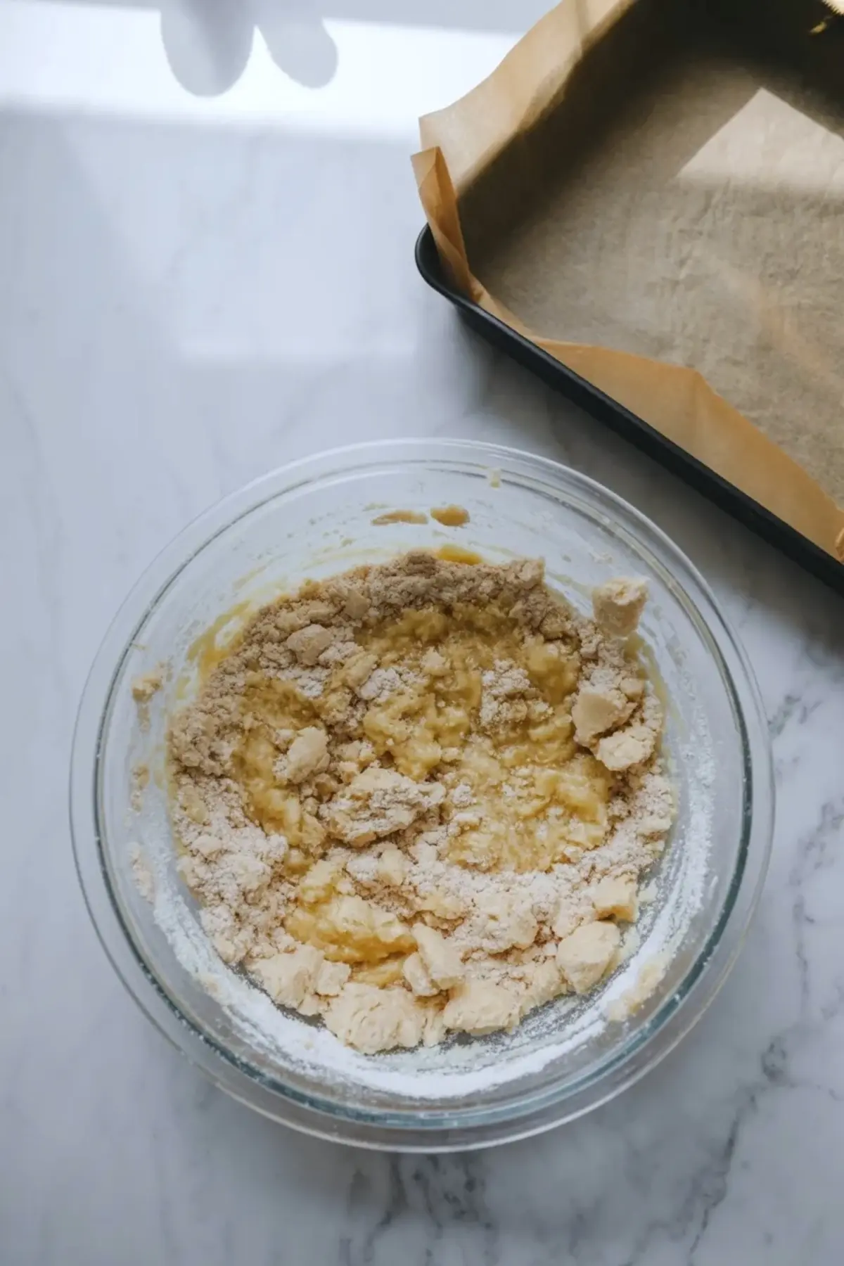 Crumb mixture in a glass bowl beside a lined baking pan for blueberry cheesecake crumb bars.