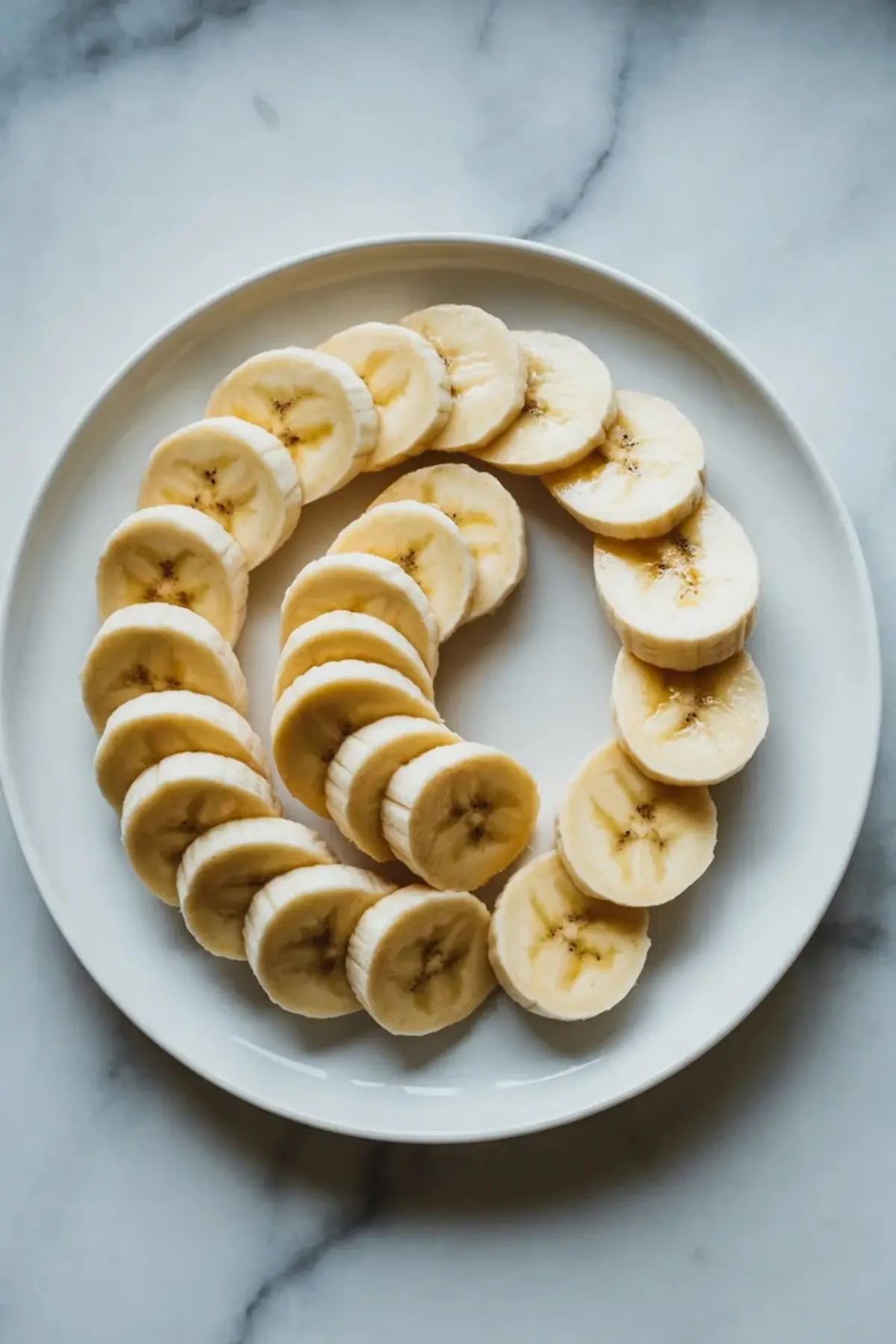 Banana slices arranged on a white plate for caramelized banana recipe before cooking.