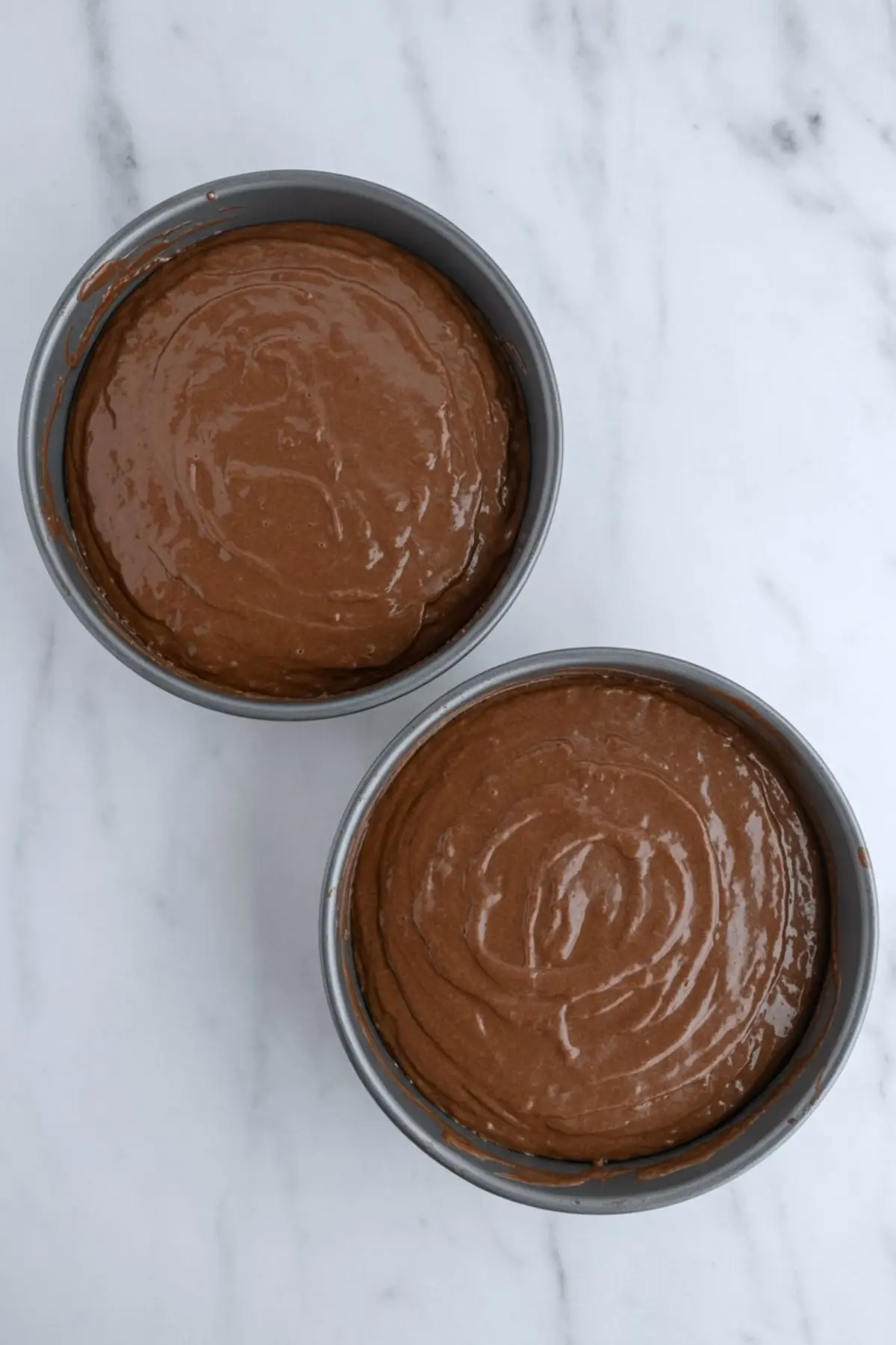 Chocolate cake batter is portioned into round cake pans for baking a layered chocolate cherry cake.