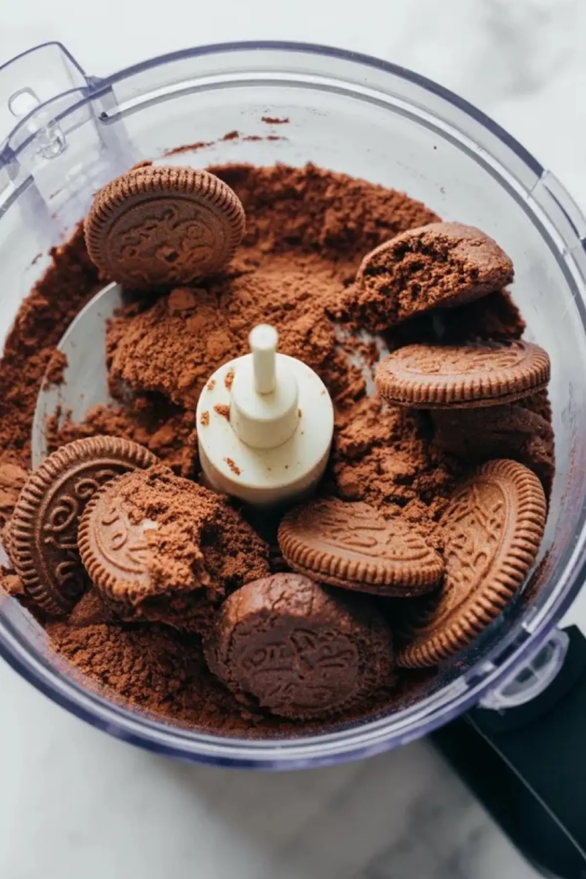 Food processor crushes chocolate sandwich cookies into fine crumbs to create a chocolate cookie crust for a coffee cheesecake dessert recipe.
