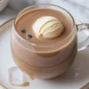 A glass mug of coffee punch sits on a white saucer topped with a scoop of vanilla ice cream.