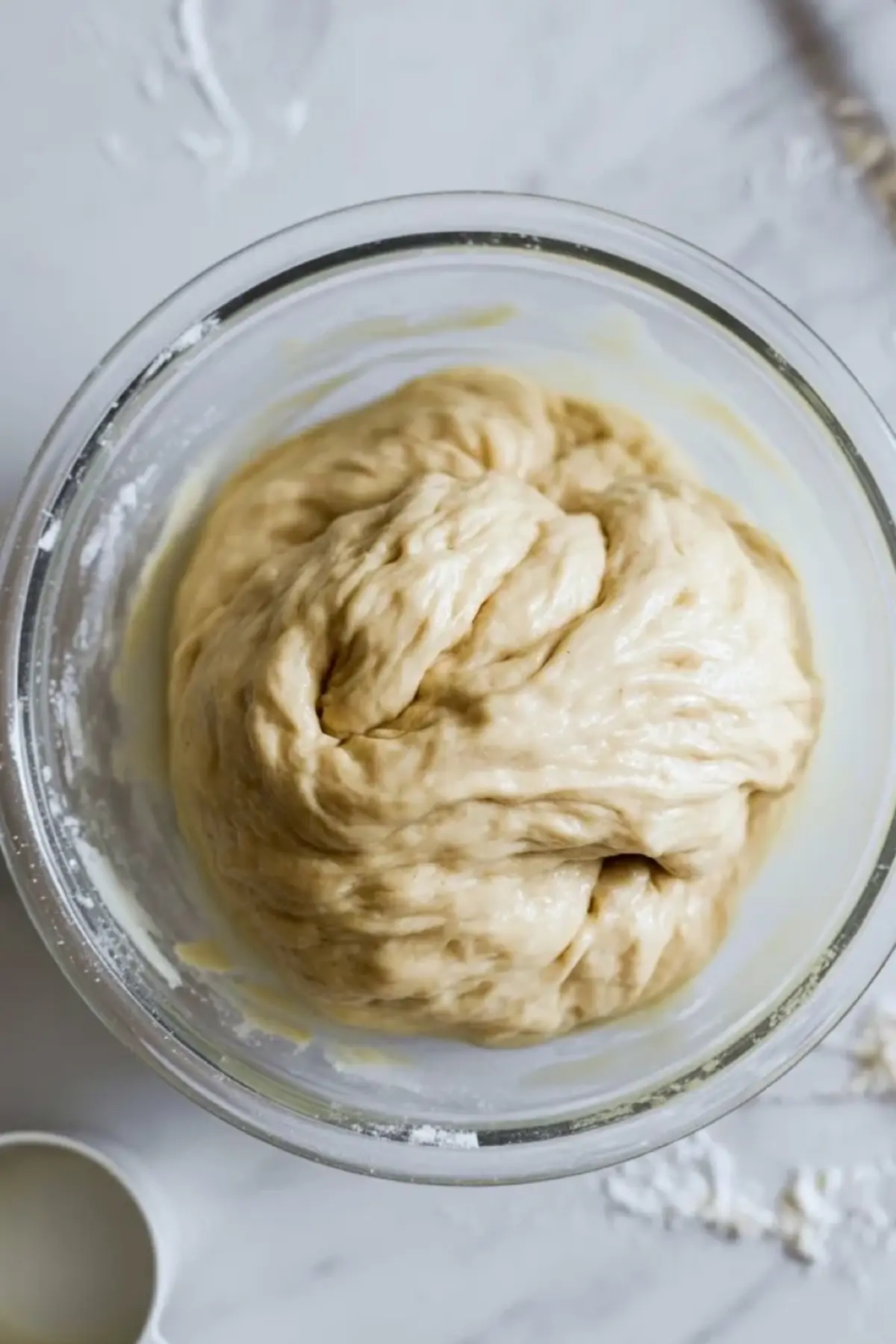 Soft condensed milk bread dough resting in a glass bowl on a marble surface.