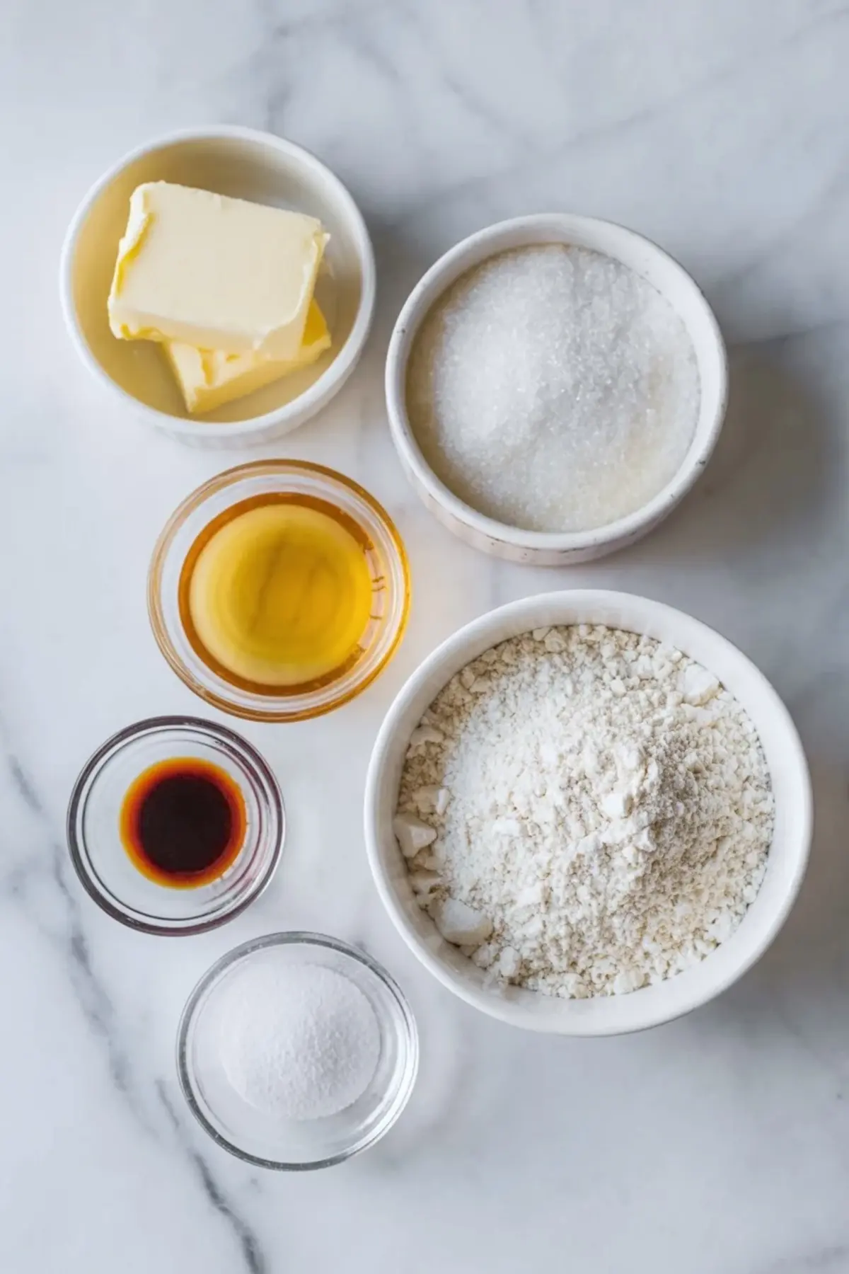 Small bowls display butter, granulated sugar, sweetened condensed milk, vanilla extract, flour, and baking powder on a marble countertop. The measured ingredients prepare a simple homemade cookie recipe.